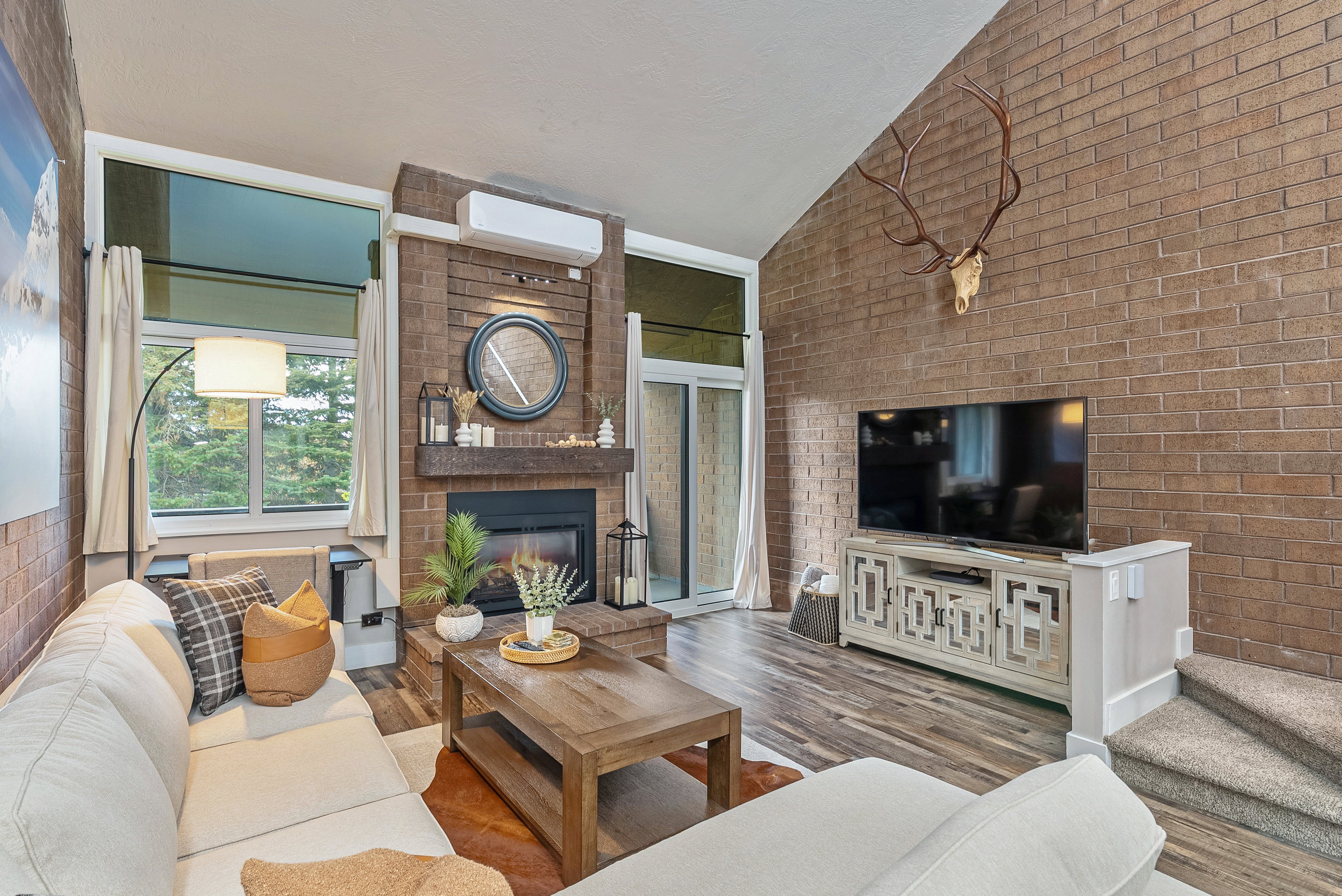Living area featuring a floor-to-ceiling brick fireplace with a wood mantel, vaulted ceiling, wood-finish flooring, and a sliding glass door