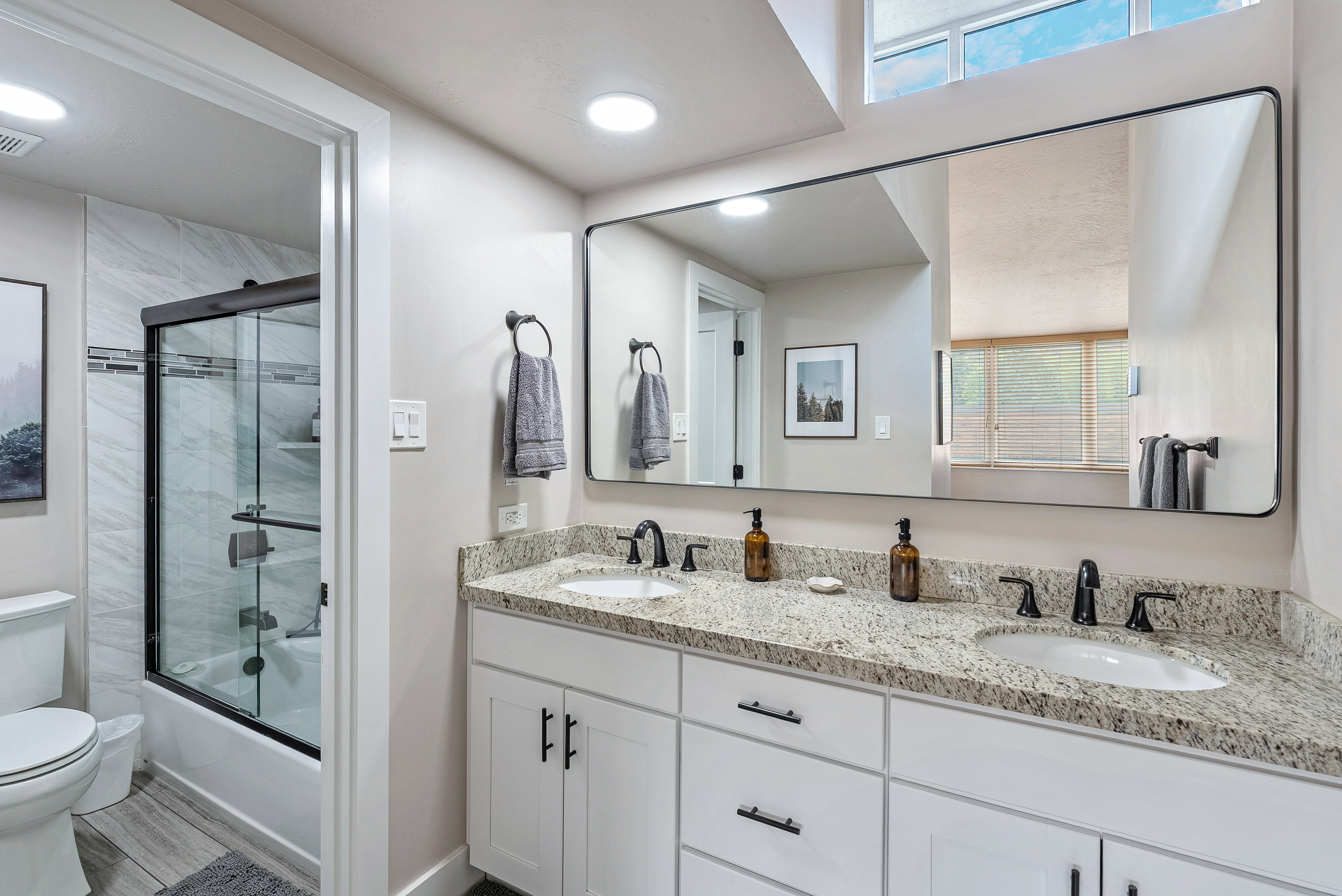 Bathroom featuring a dual vanity with light granite countertops, white cabinetry, and matte black hardware