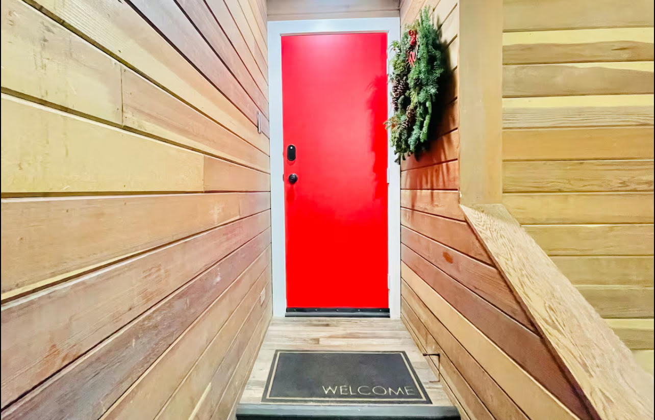 Vibrant red entry door framed by light wood-finish siding walls