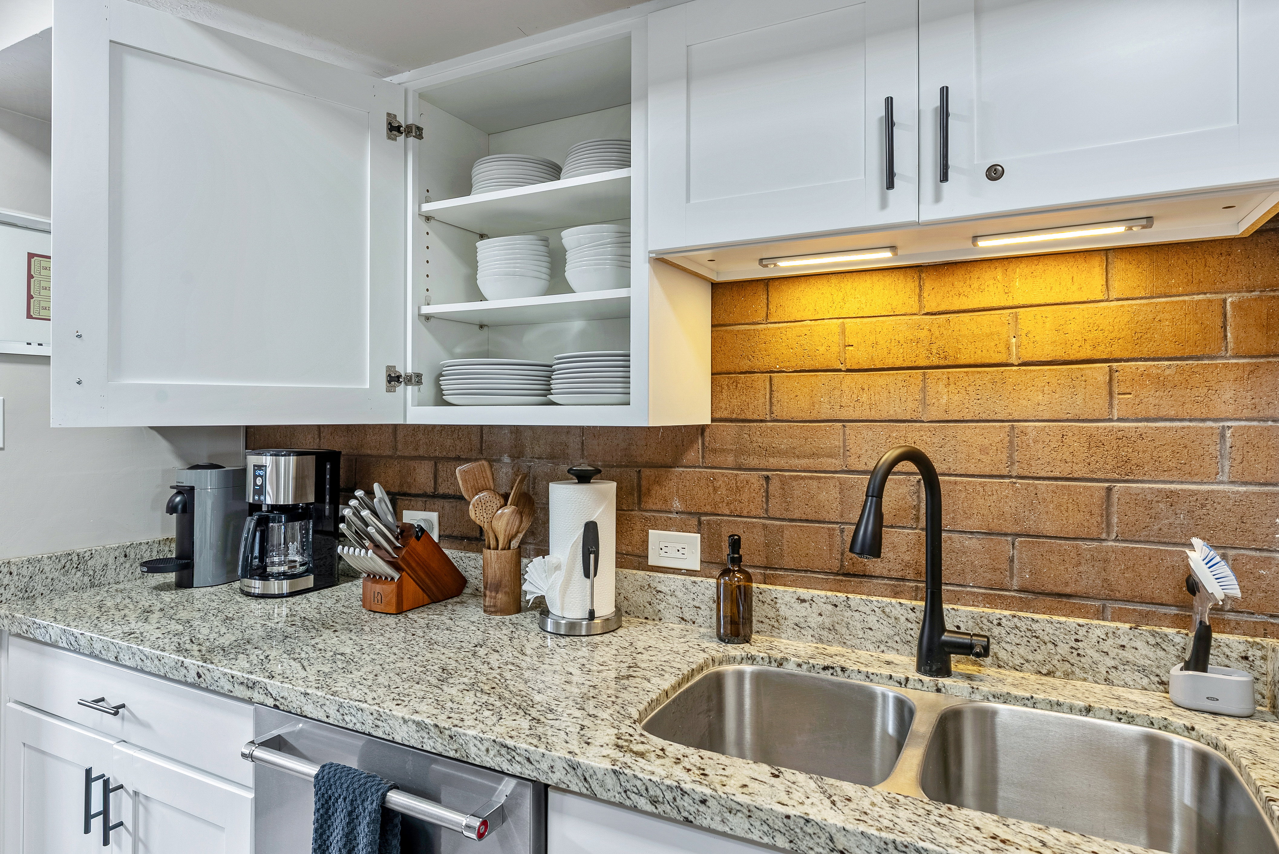 Kitchen featuring white shaker-style cabinetry, granite-finish countertops, and a brick-look backsplash