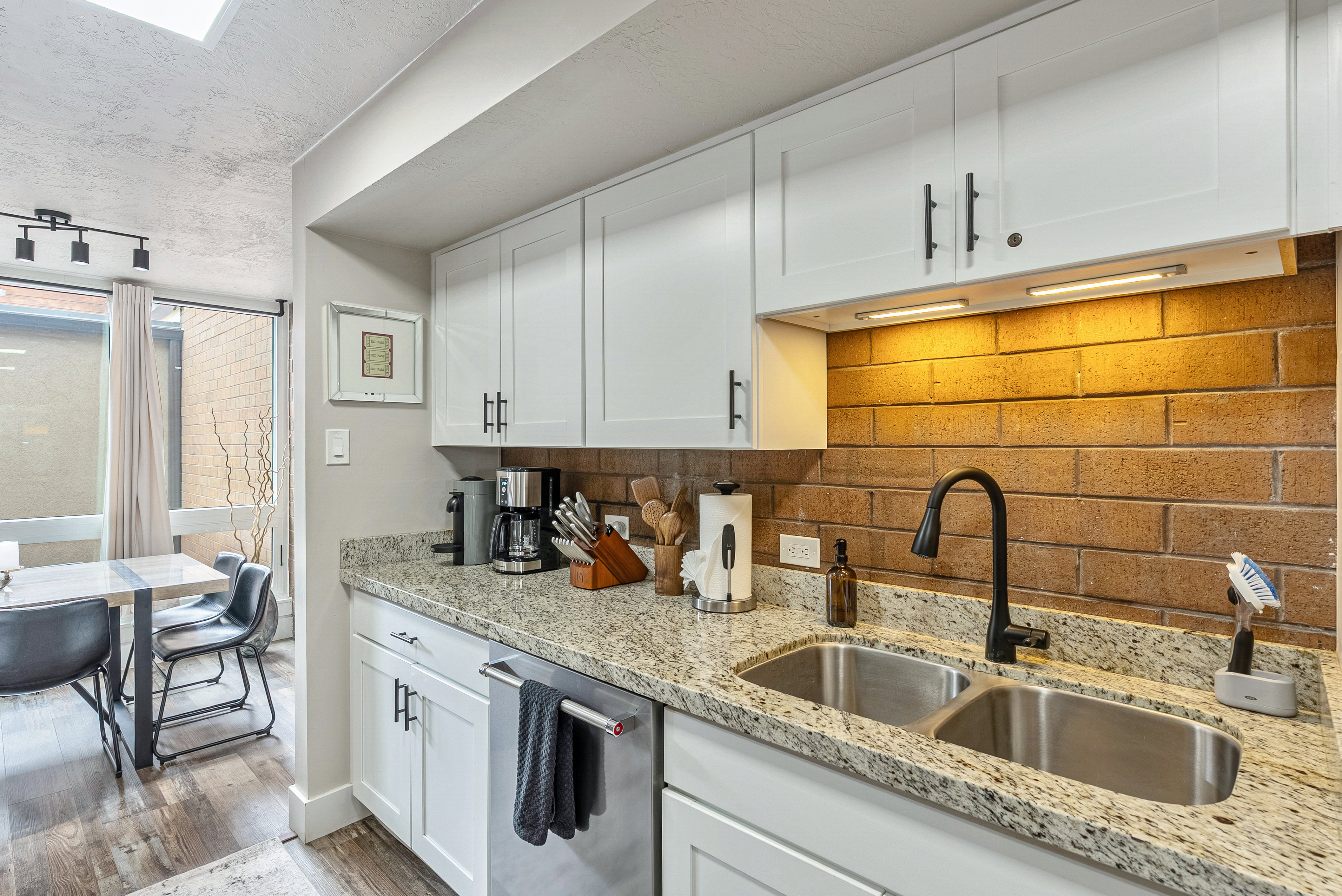 Kitchen featuring white shaker cabinetry, granite-finish countertops, and a brick-finish backsplash