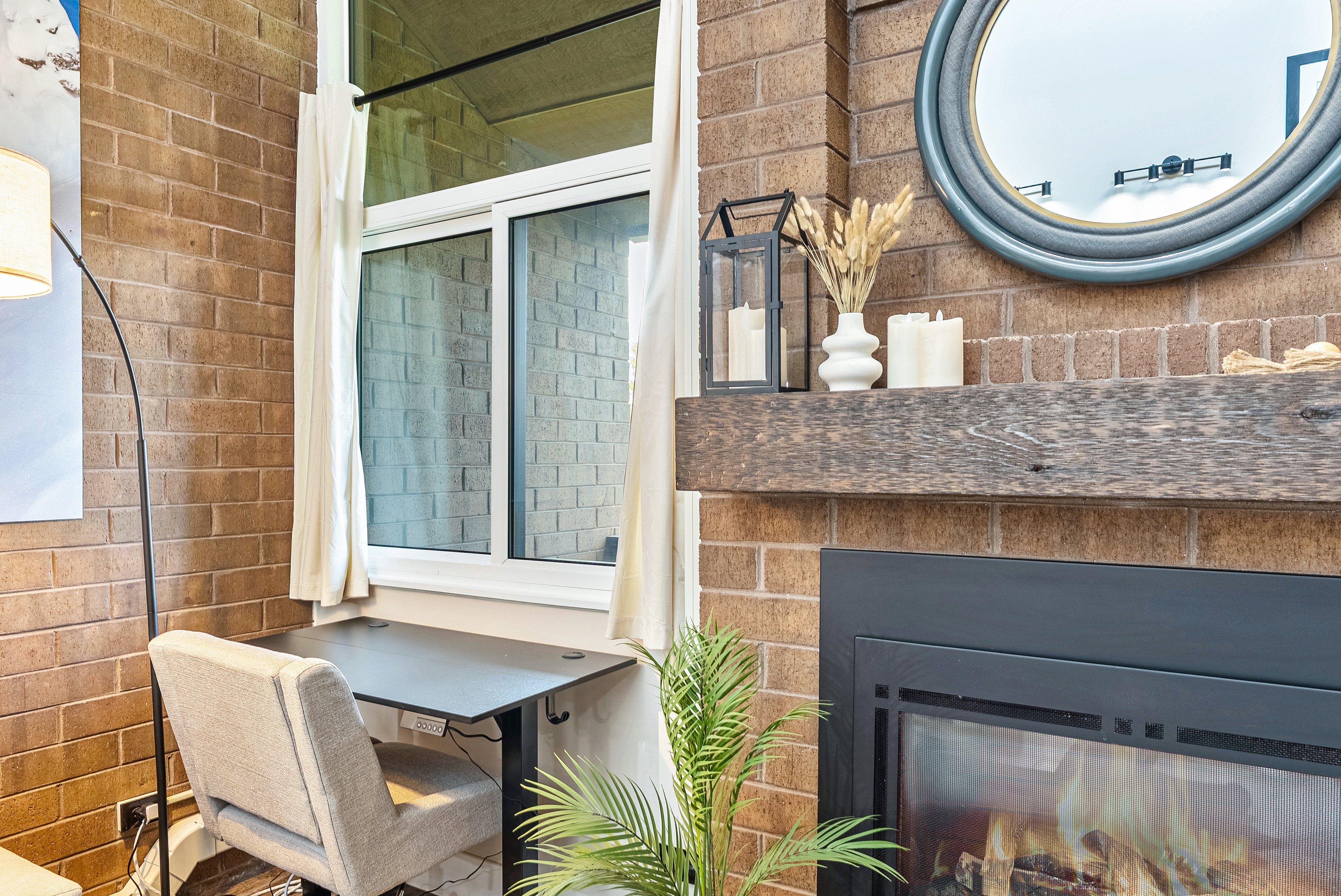 Exposed brick wall with an integrated fireplace featuring a substantial wood mantel