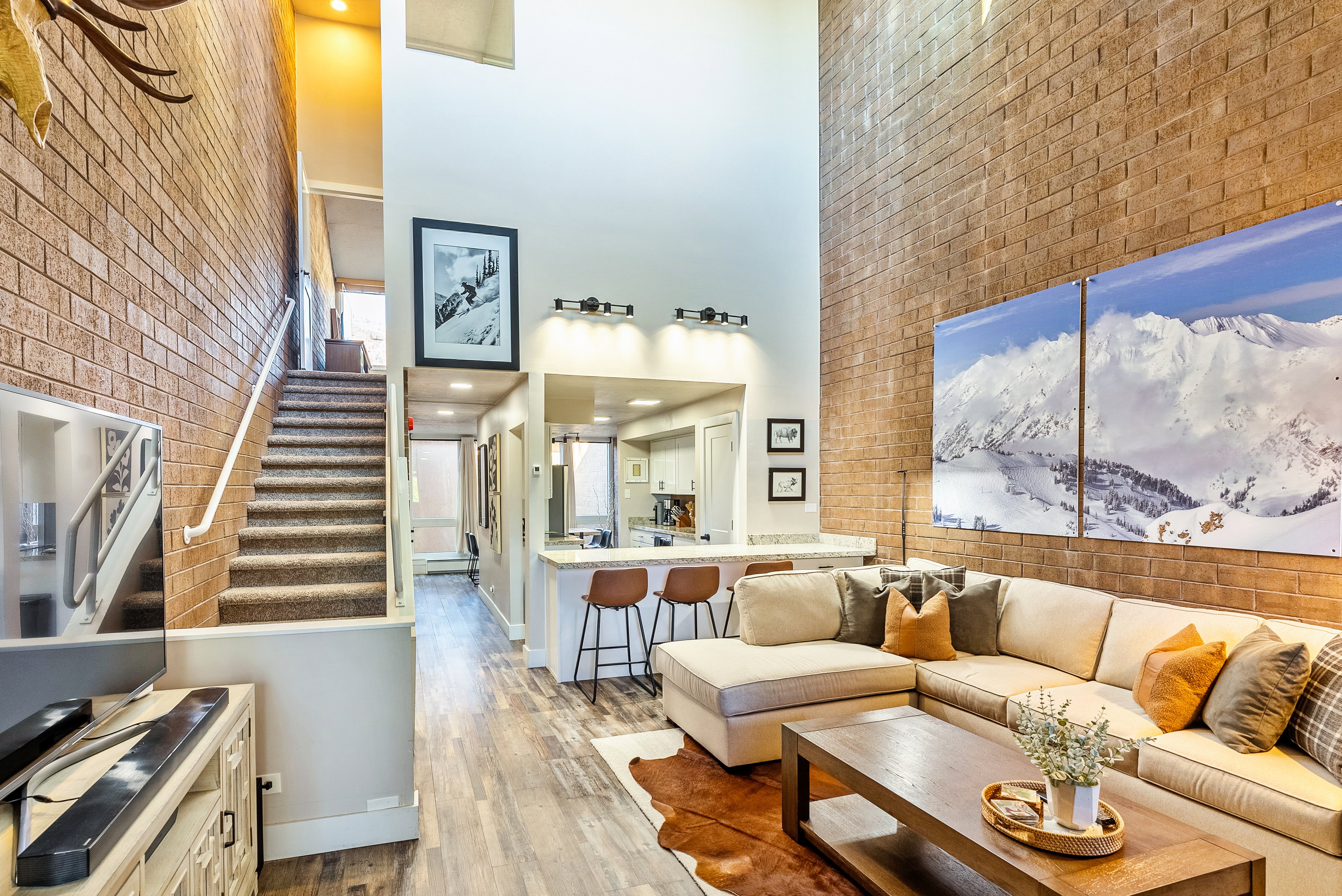 Living area featuring a soaring ceiling, exposed brick accent wall, wood-finish flooring, and a breakfast bar with stone-look countertop