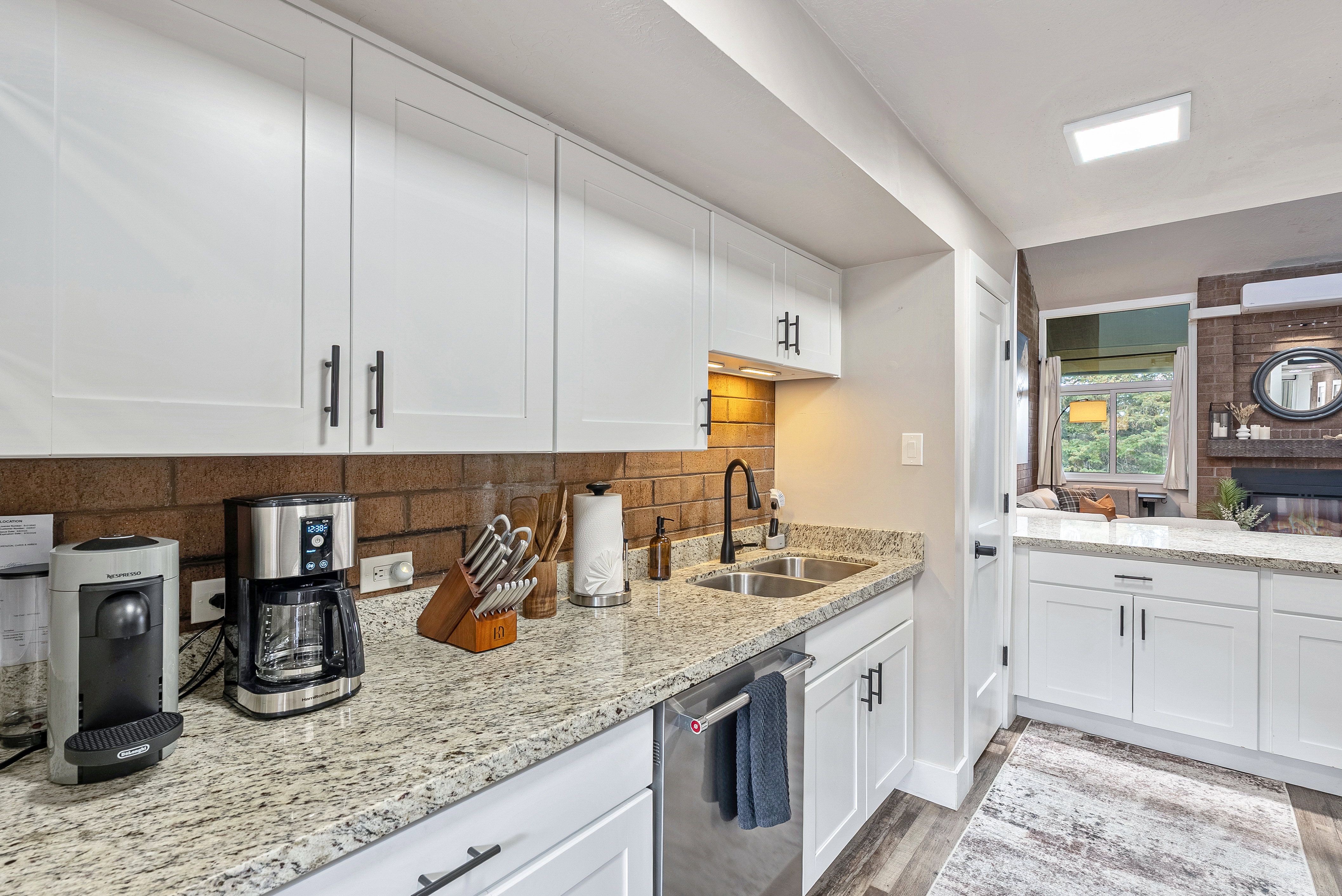 Contemporary kitchen featuring white cabinetry with matte black hardware, granite-style countertops, a brick-patterned backsplash, and a double basin stainless steel sink with a matte black faucet