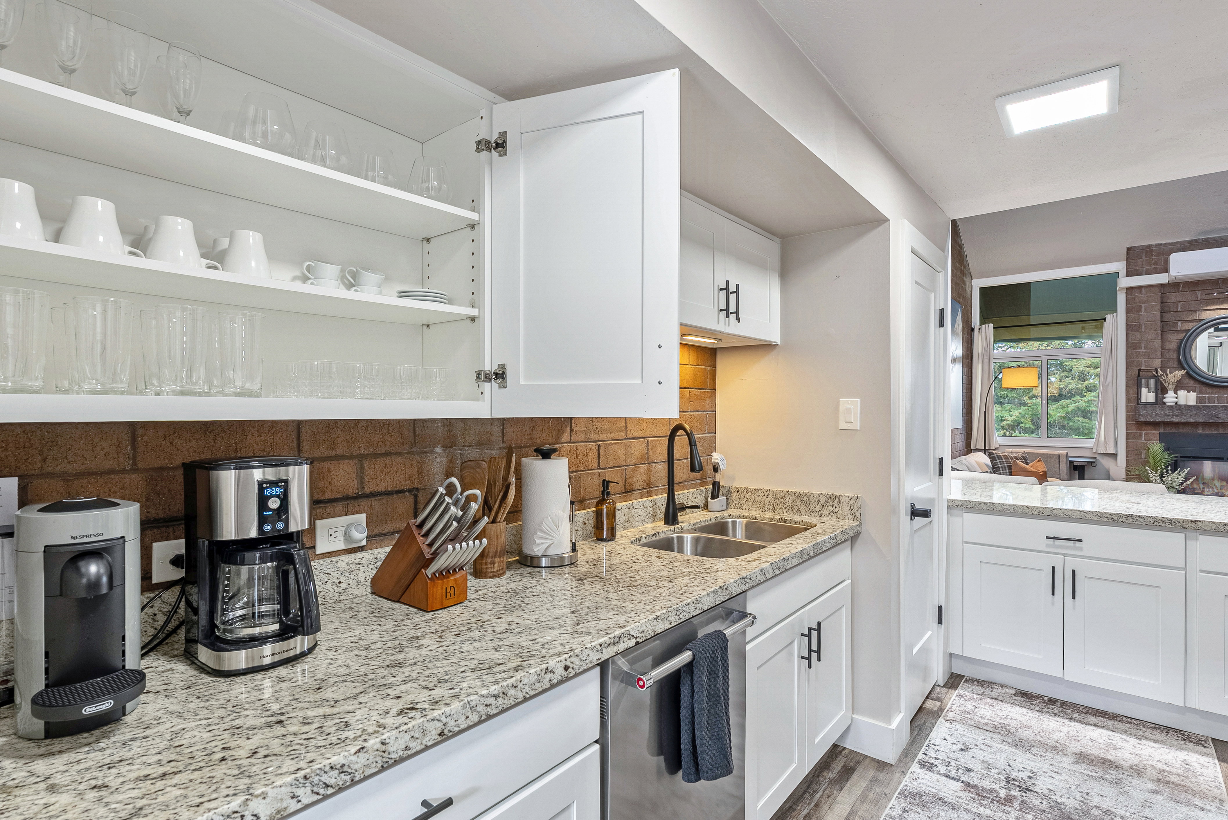 Kitchen featuring white cabinetry with black hardware, a dual-basin stainless steel sink, granite-finish countertops, and a brick-finish backsplash