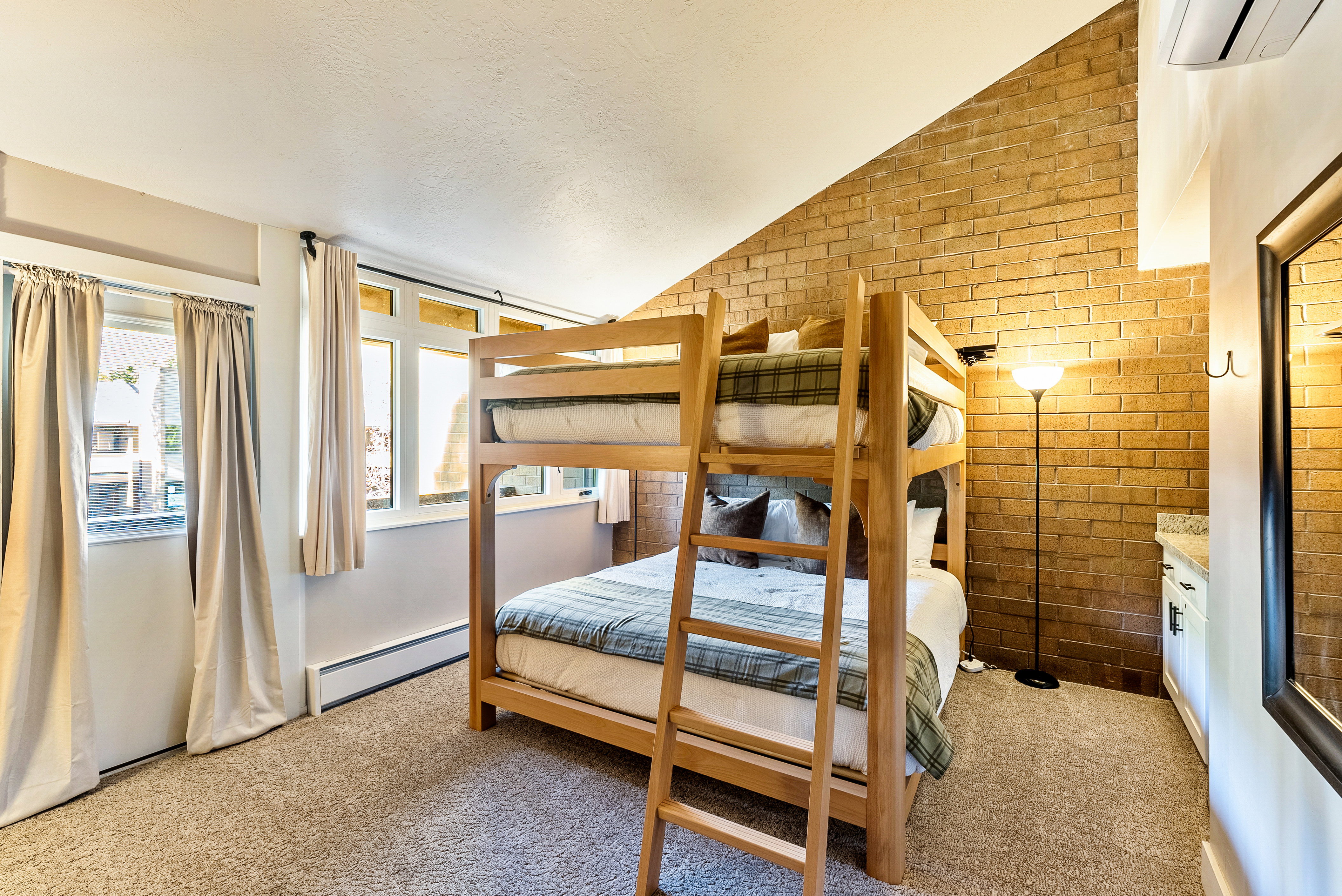 Angled brick accent wall with bunk beds, carpeted flooring, and multiple windows