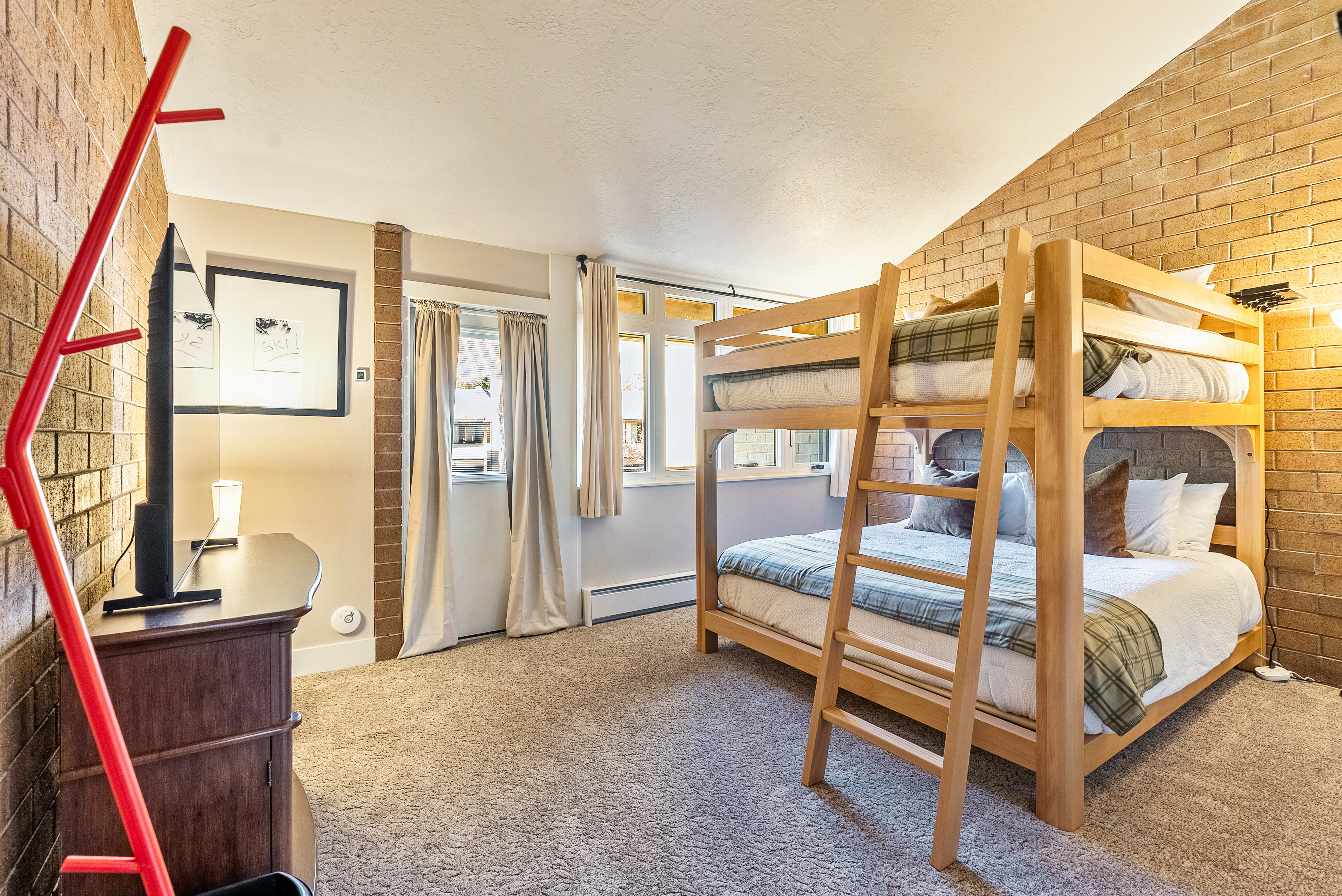 Accommodating room featuring a wooden bunk bed, light brown brick accent walls, and neutral-toned carpeting