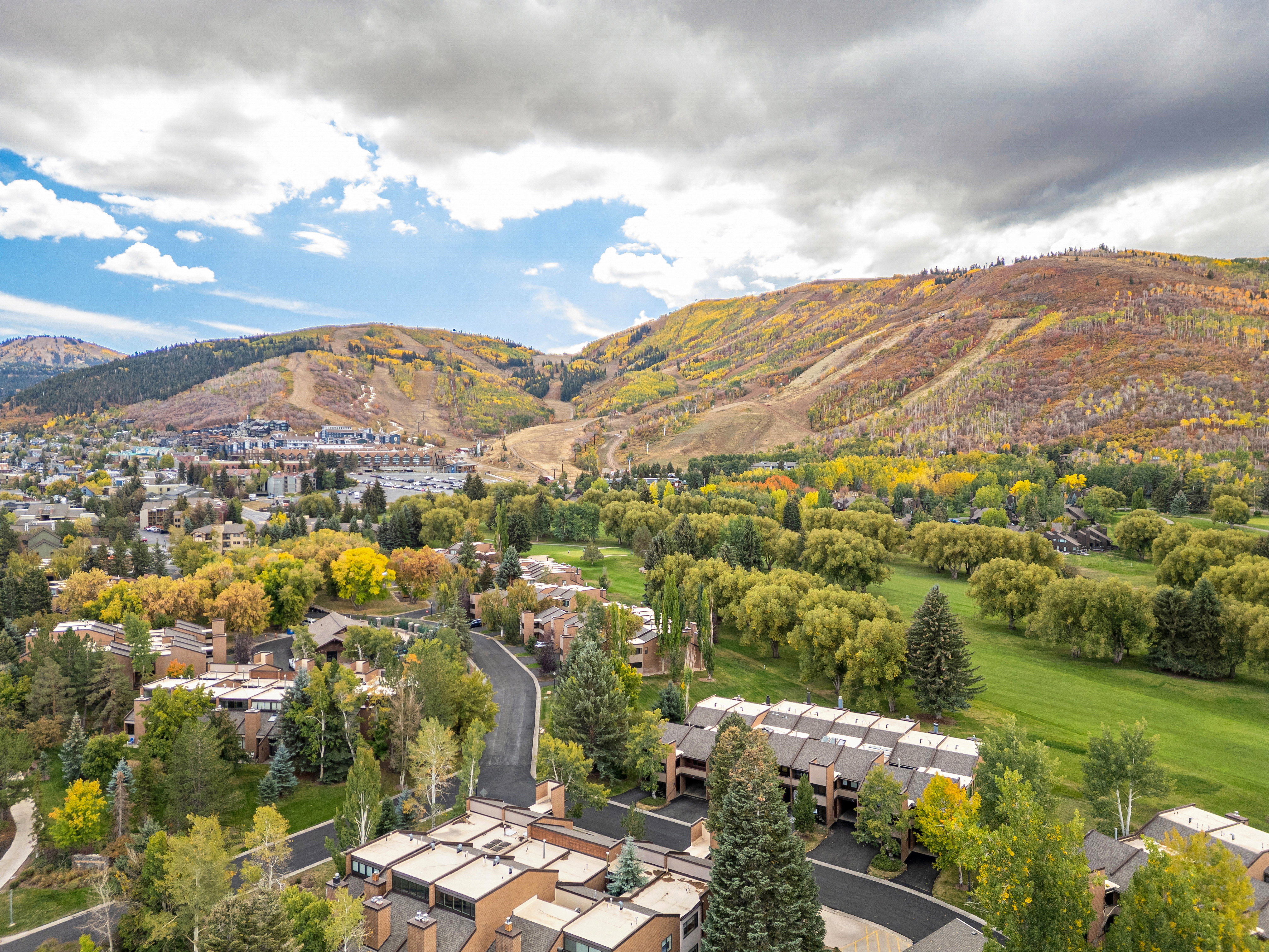 Aerial landscape featuring residential properties set against a backdrop of mountainous terrain with autumnal foliage and a green golf course