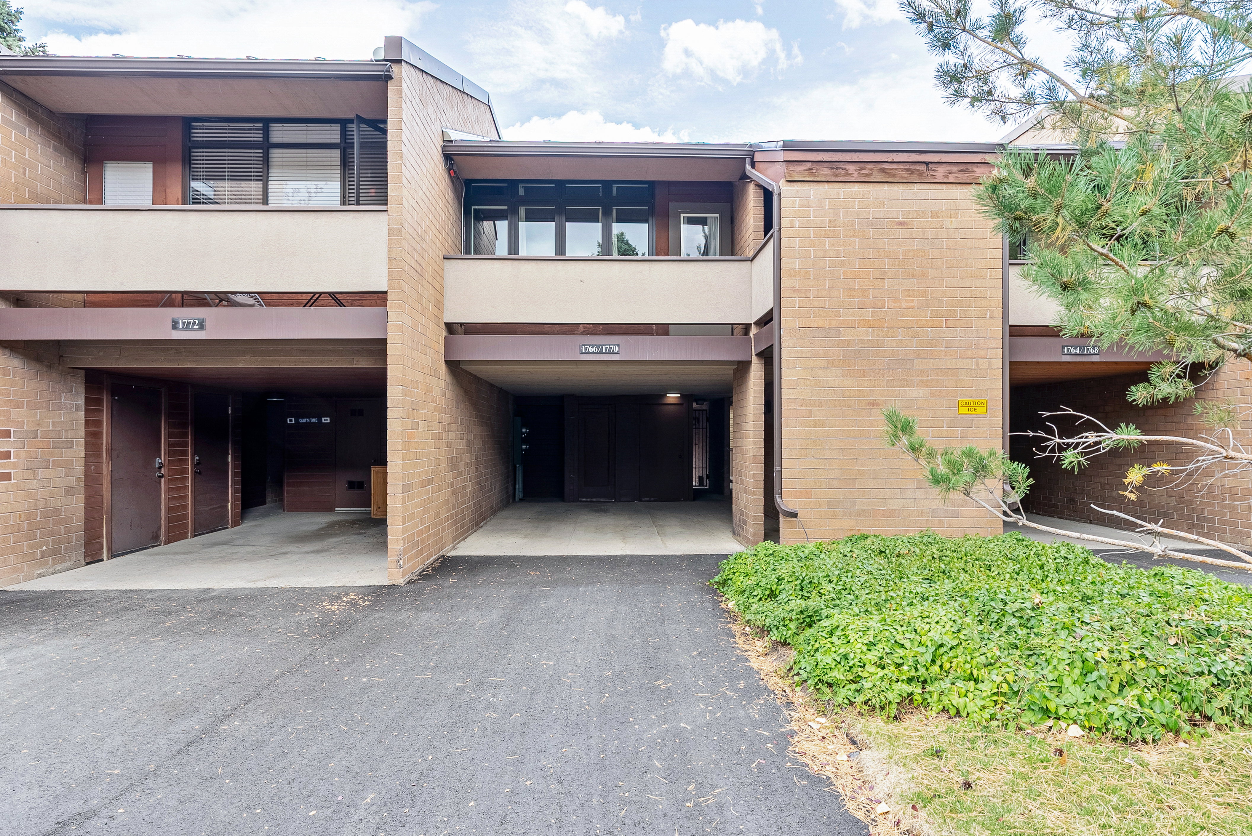 Multi-level brick exterior featuring covered parking, second-story balconies with dark window frames, and mature landscaping