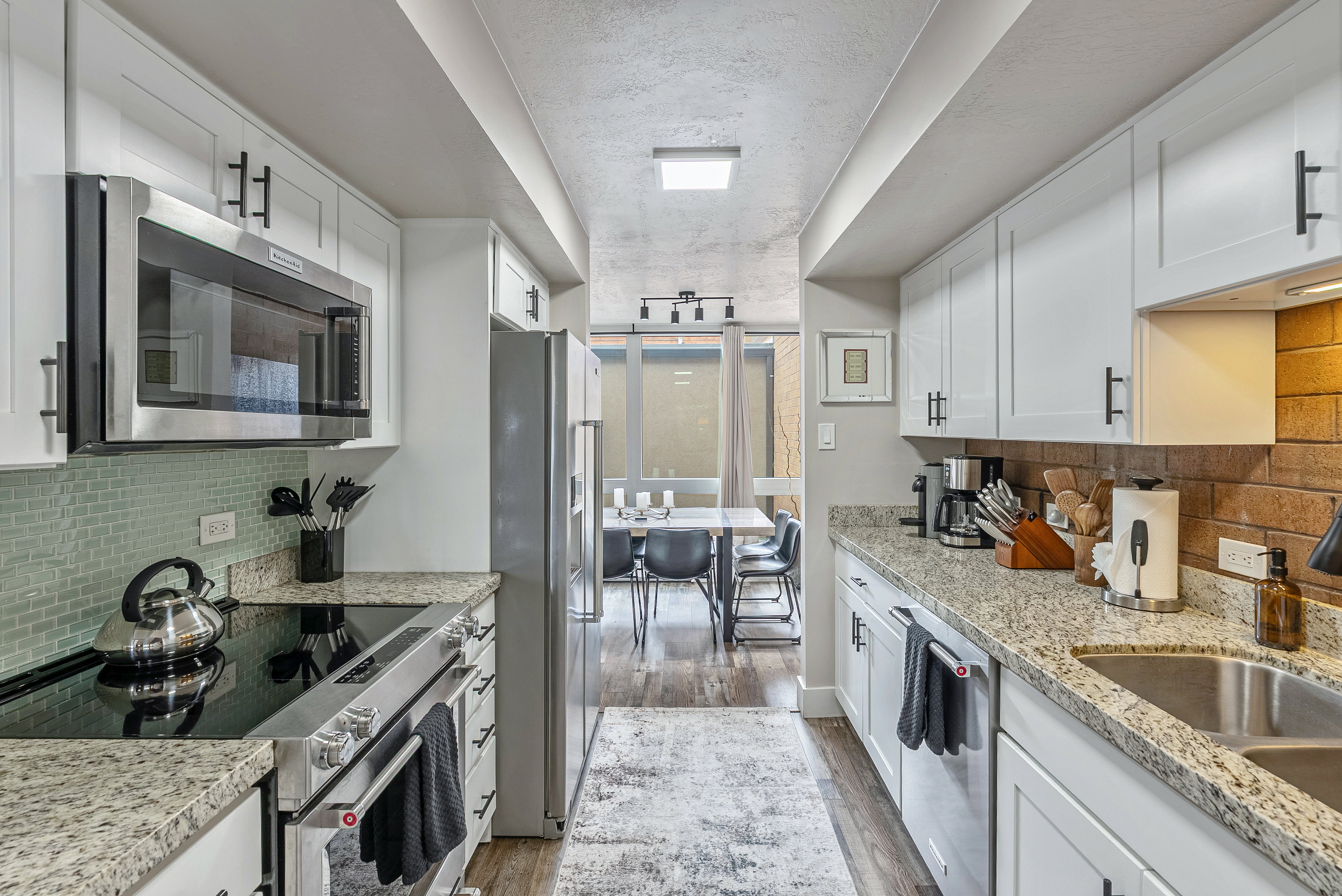 Galley kitchen featuring white shaker cabinetry with black hardware, stainless steel appliances including an over-the-range microwave and electric range, and granite countertops