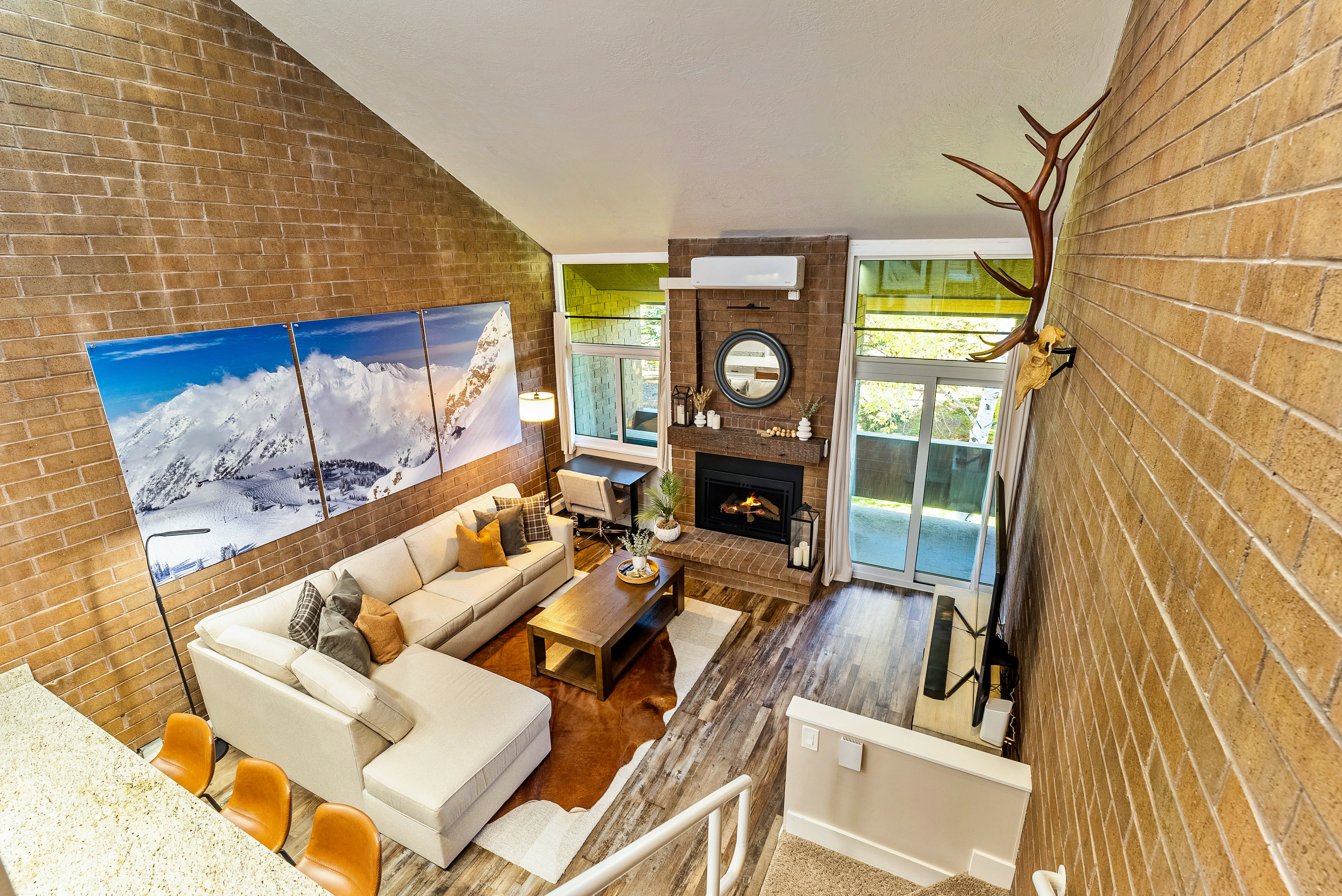 Great room featuring vaulted ceilings, a brick accent wall, wood-finish flooring, and a fireplace with a wood mantle