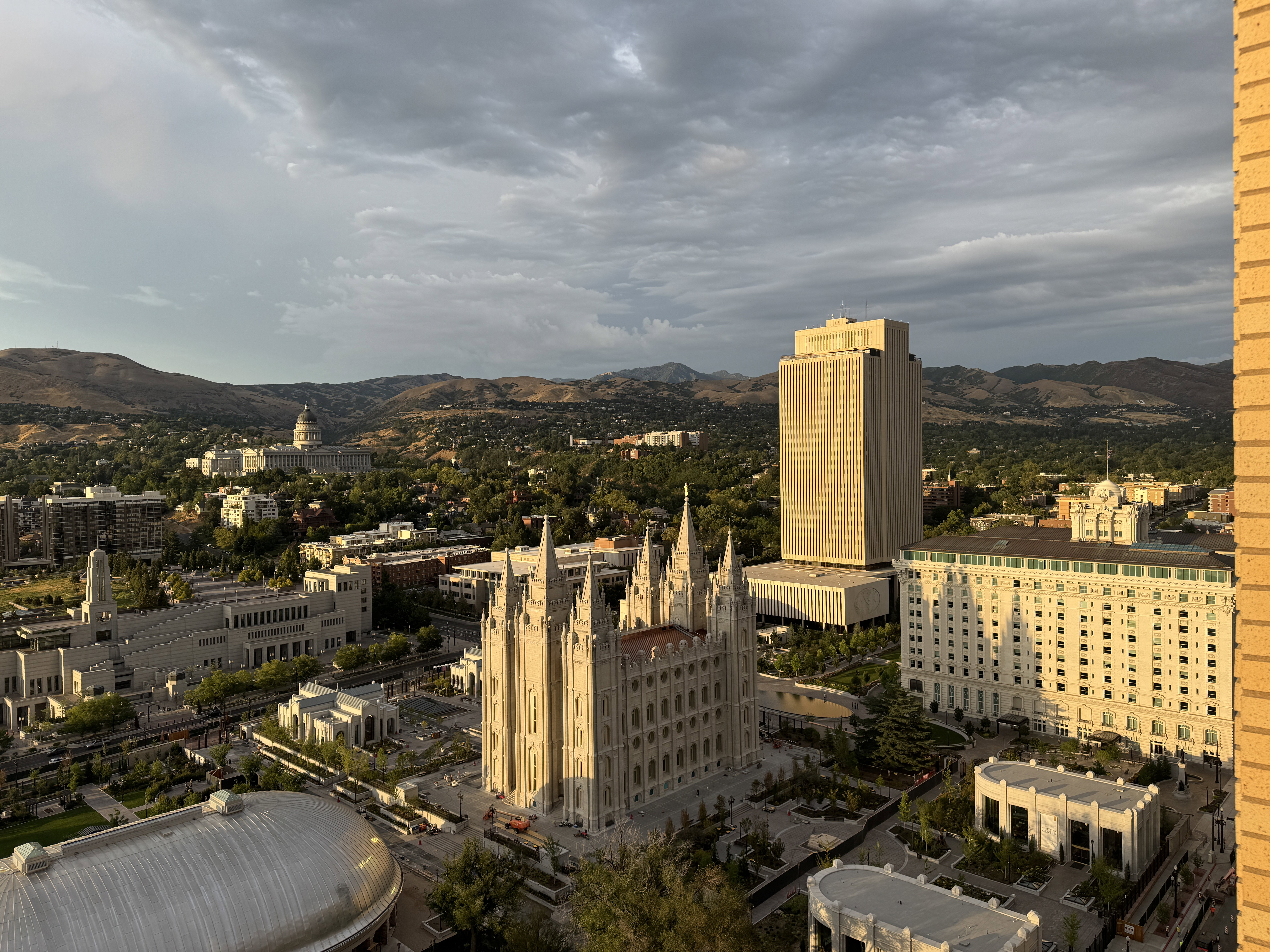 Expansive cityscape featuring prominent architectural landmarks, verdant tree-lined streets, and distant mountain ranges