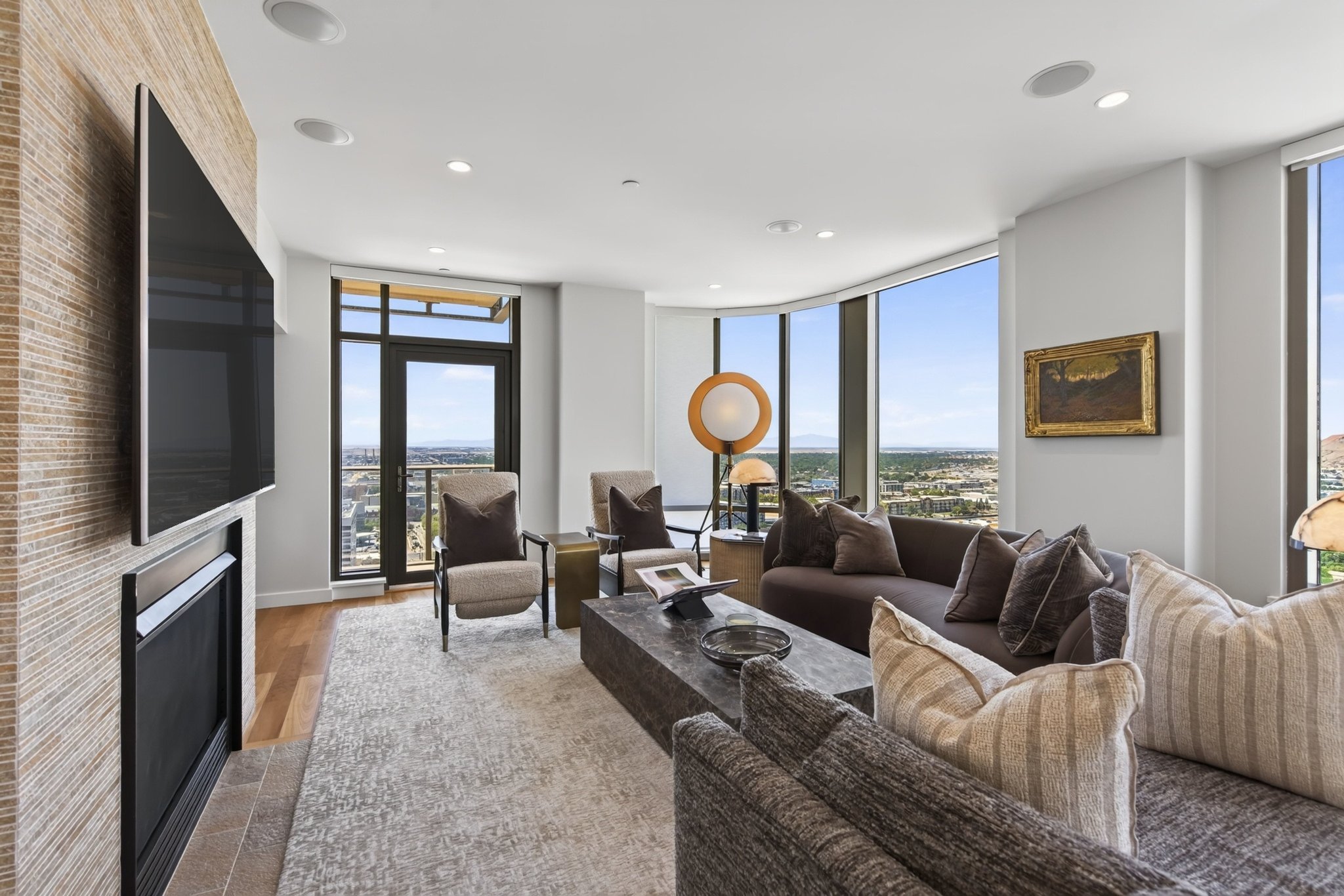 Living area featuring a contemporary fireplace with textured surround, floor-to-ceiling windows, recessed lighting, wood-finish flooring, and a glass-paneled door opening to an outdoor space