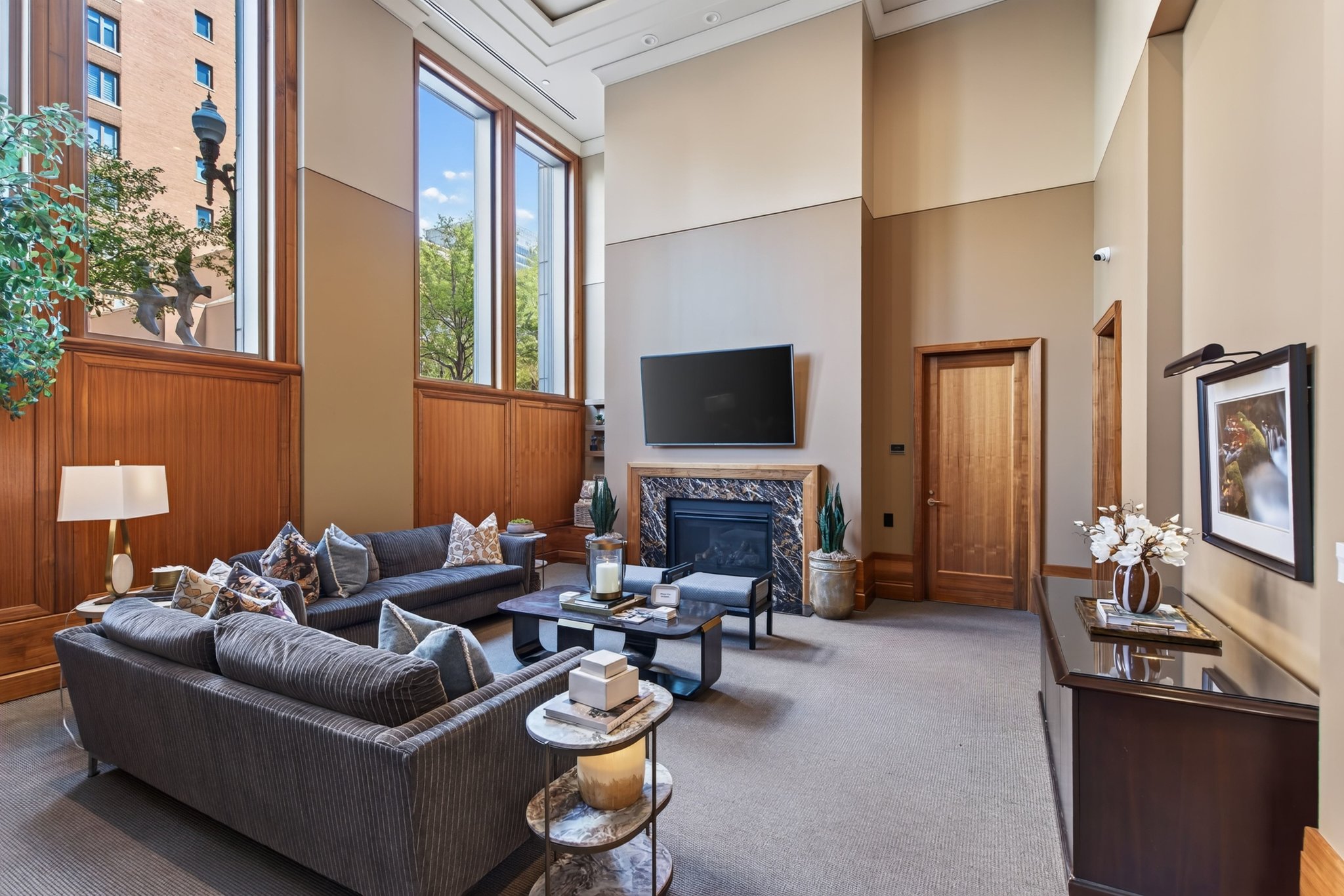 Spacious living area featuring double-height ceilings, a fireplace with a stone surround, and tall windows with wood paneling