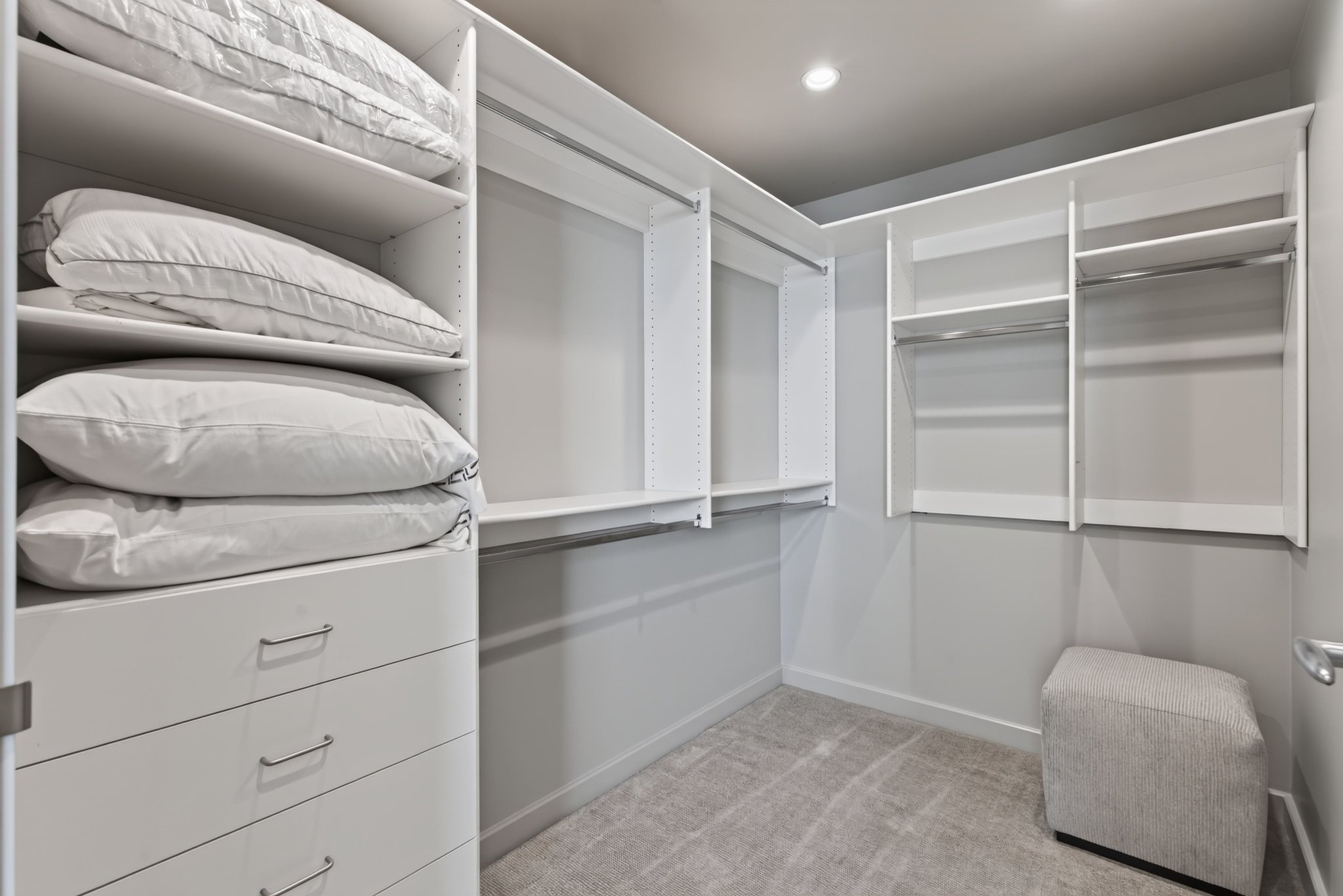 Custom closet system featuring white shelving units, multiple hanging rods, built-in drawers with modern hardware, and recessed ceiling lighting