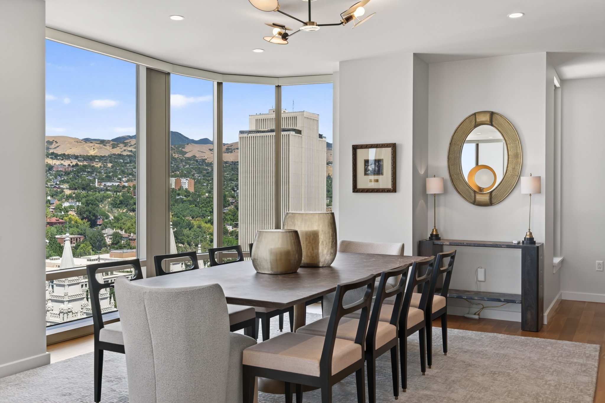 Dining area with extensive floor-to-ceiling windows, modern chandelier lighting, light wood-finish flooring, and a contemporary console table