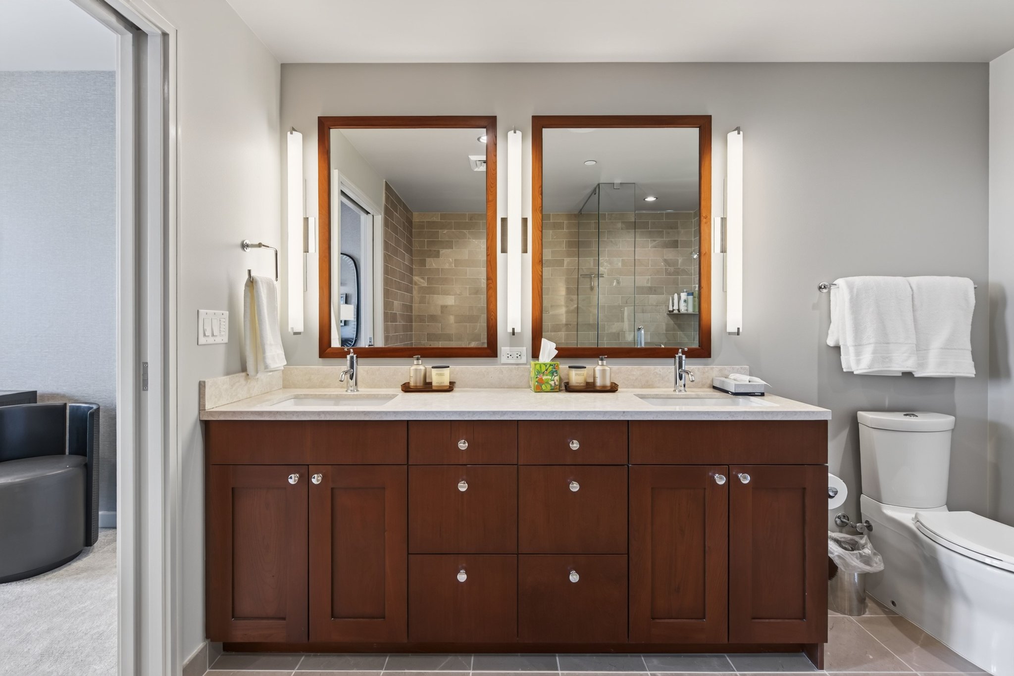Dual vanity with stone countertop, integrated sinks, wood-finish cabinetry, and framed mirrors with vertical sconce lighting