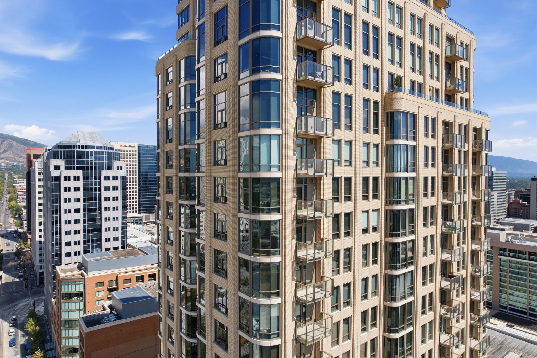High-rise building featuring a light-toned facade, numerous balconies with glass railings, expansive windows, and curved architectural elements
