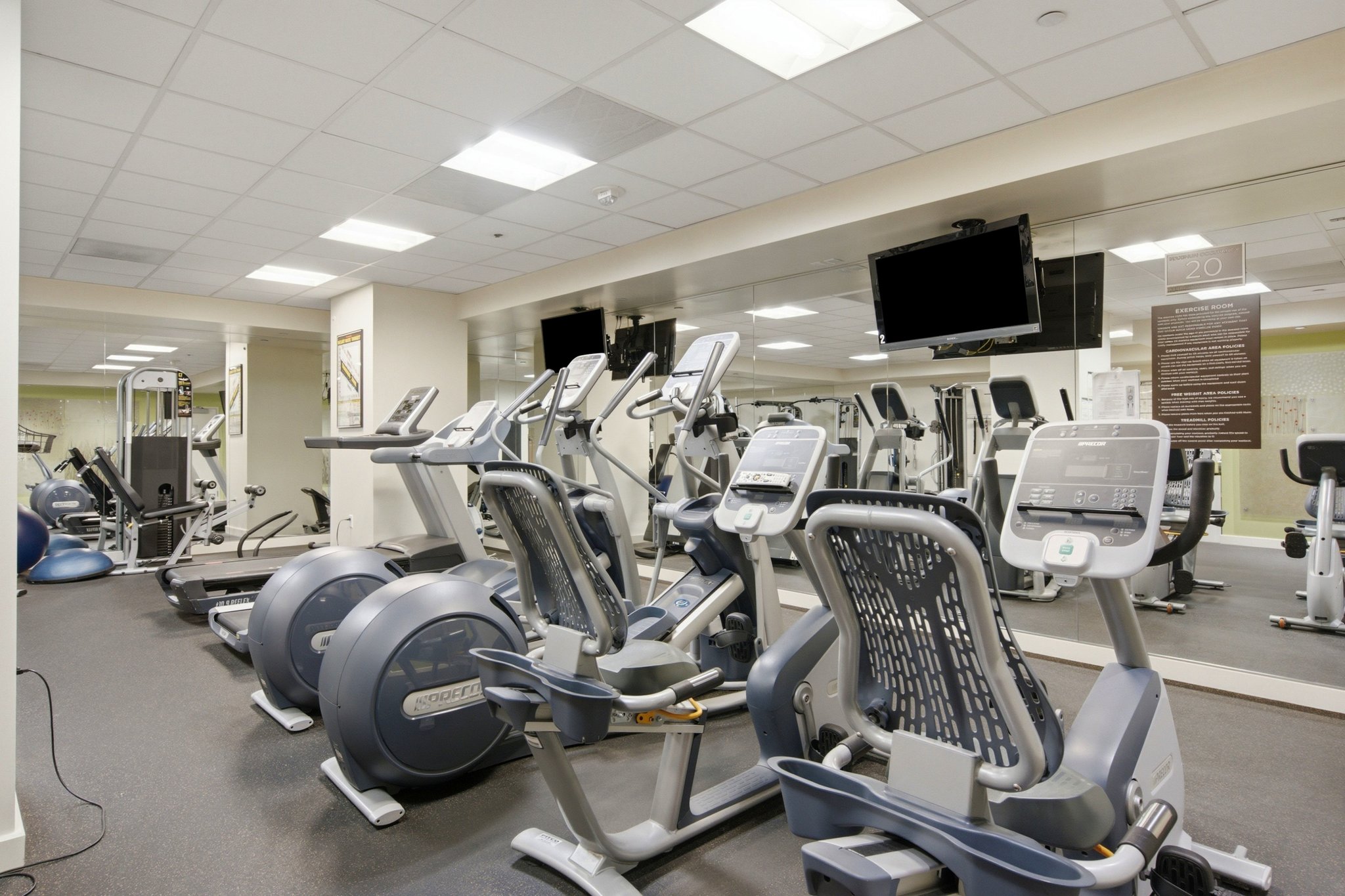 Fitness center featuring multiple exercise machines, mirrored wall, mounted television, recessed lighting, and rubberized flooring