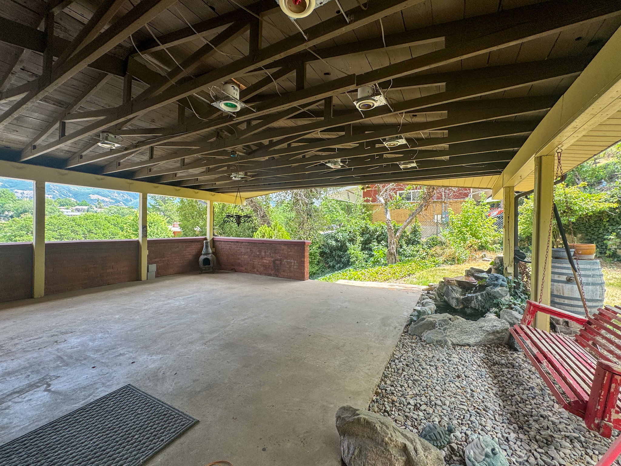 Expansive covered patio featuring a concrete floor, exposed wood beam ceiling, and a low brick wall
