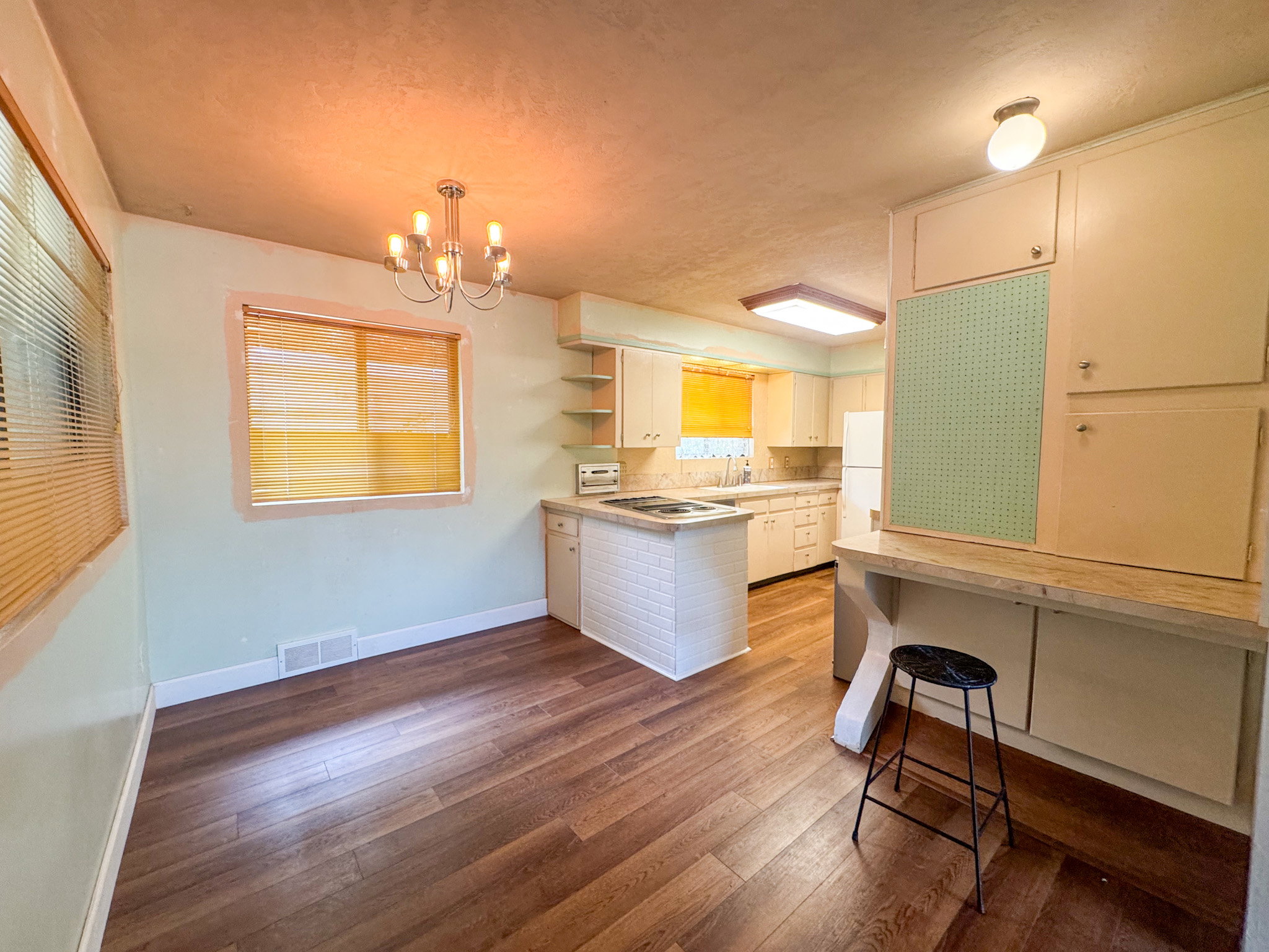 Kitchen and dining area featuring wood-finish flooring, a contemporary chandelier, white cabinetry, and a built-in workspace