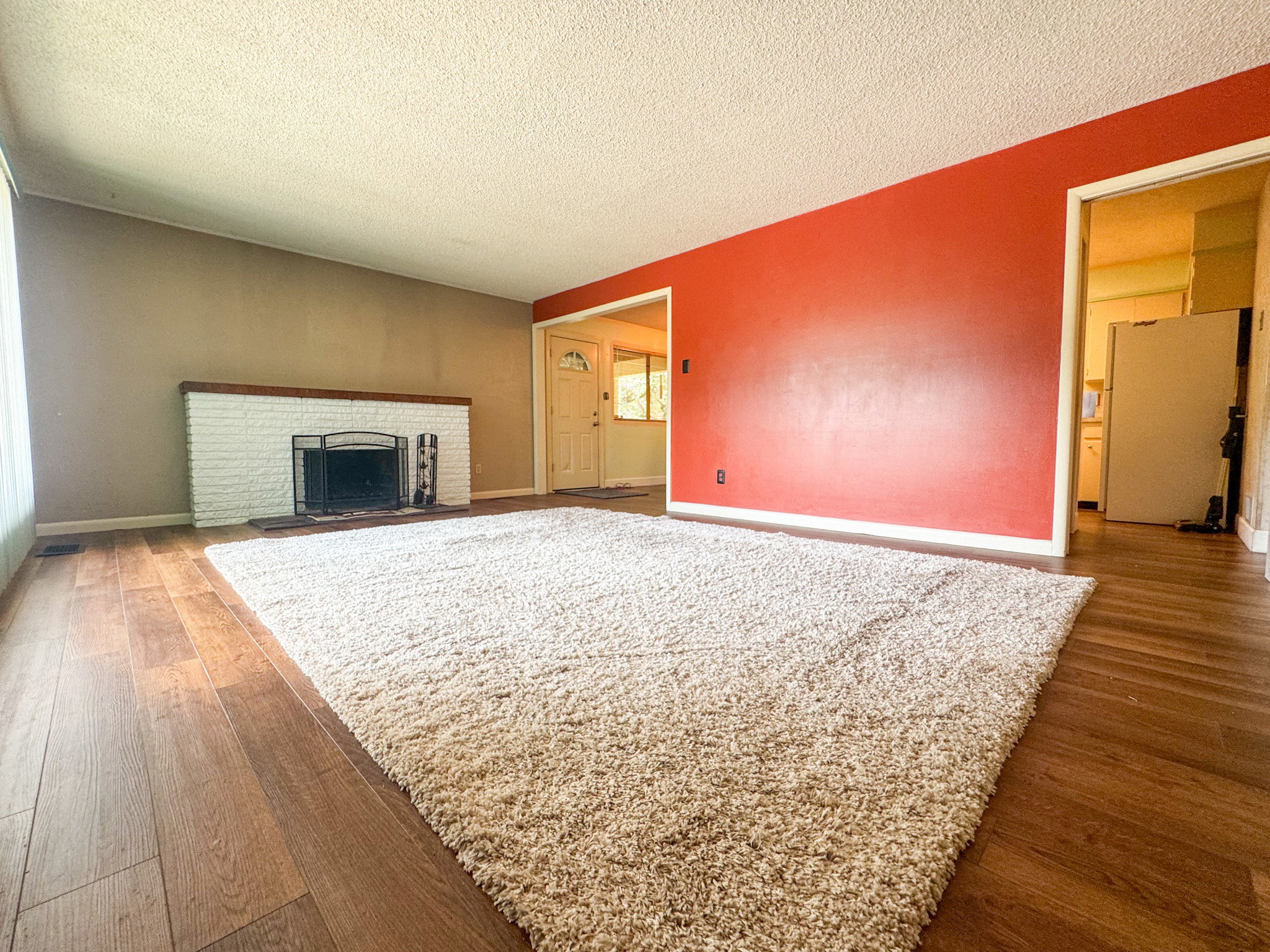 Spacious living area featuring wood-finish flooring, a white brick fireplace with a wood mantle, and an expansive area rug