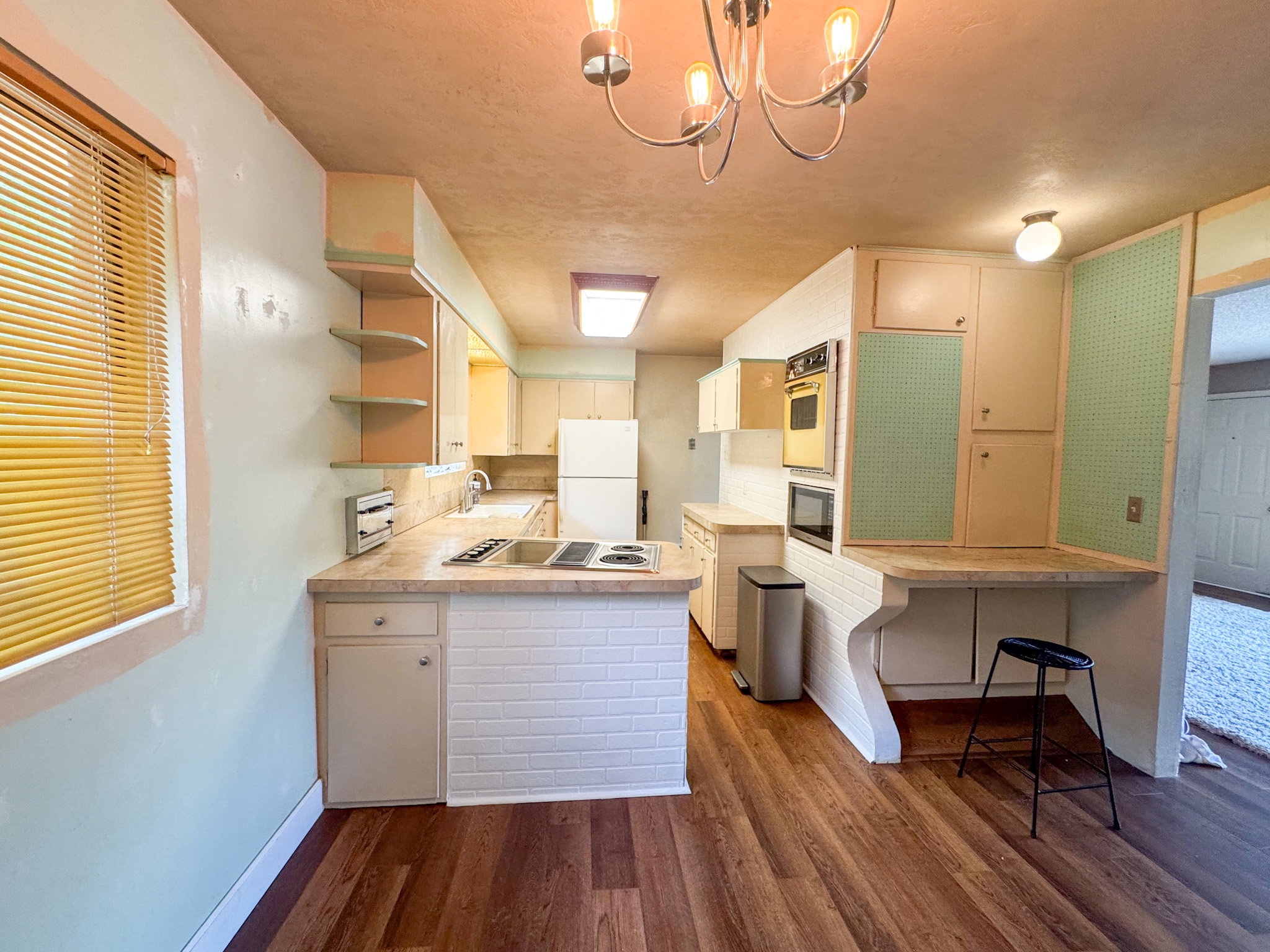 Kitchen featuring wood-finish flooring, white brick-patterned bar area, built-in wall oven and microwave, and a counter-height dining surface