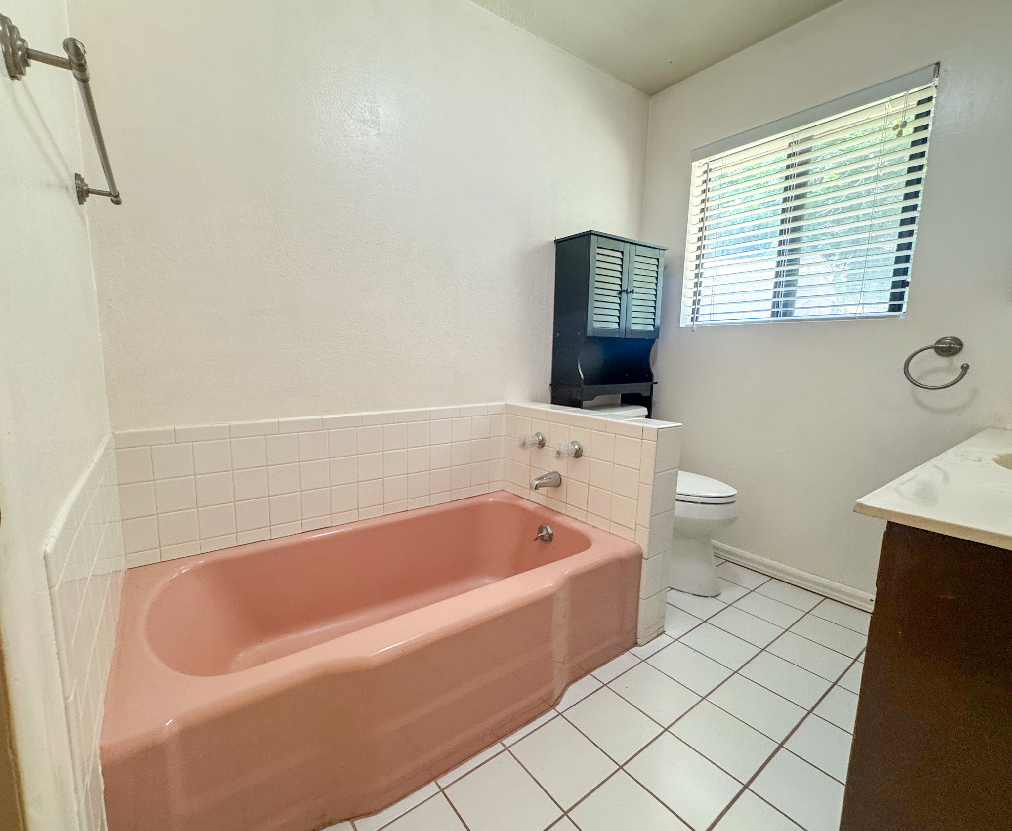 Bathroom with a pink bathtub, white tiled floor, and a window with horizontal blinds