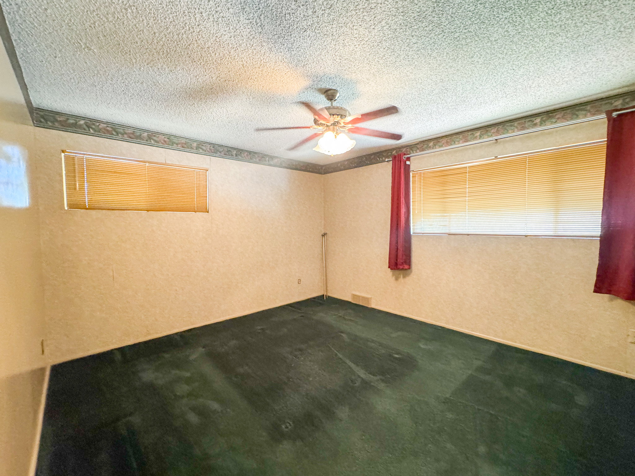 Room featuring textured wallpaper, green carpeting, a ceiling fan with integrated lighting, and two windows with horizontal blinds