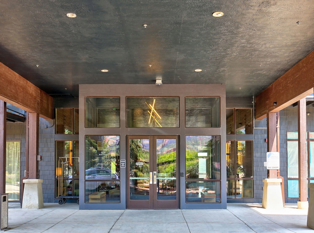 Modern entrance featuring large glass panels, double entry doors, wood-finish structural beams, and recessed lighting in the covered overhang