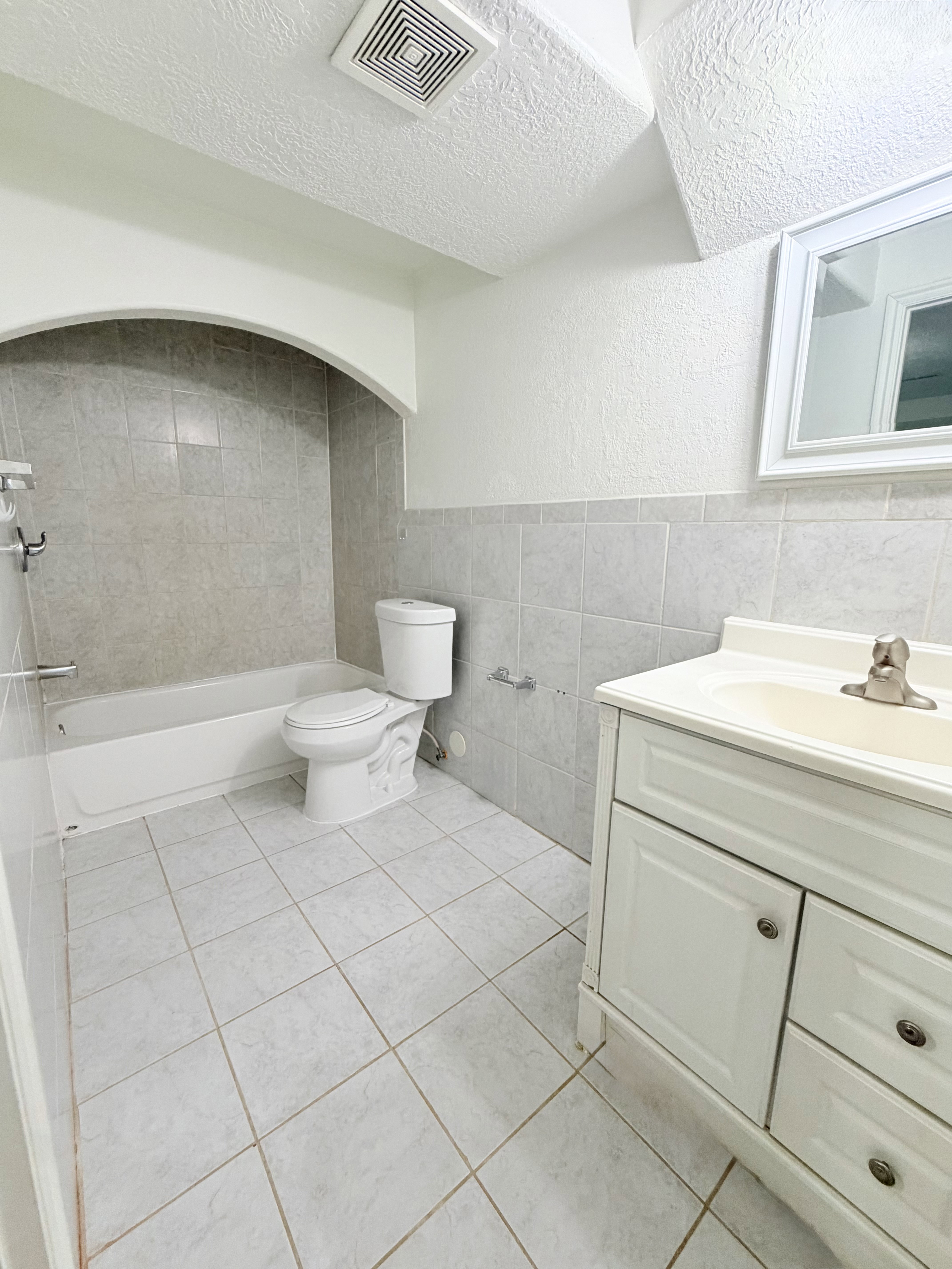 Bathroom featuring a white vanity with integrated sink, white tub, toilet, and tiled flooring