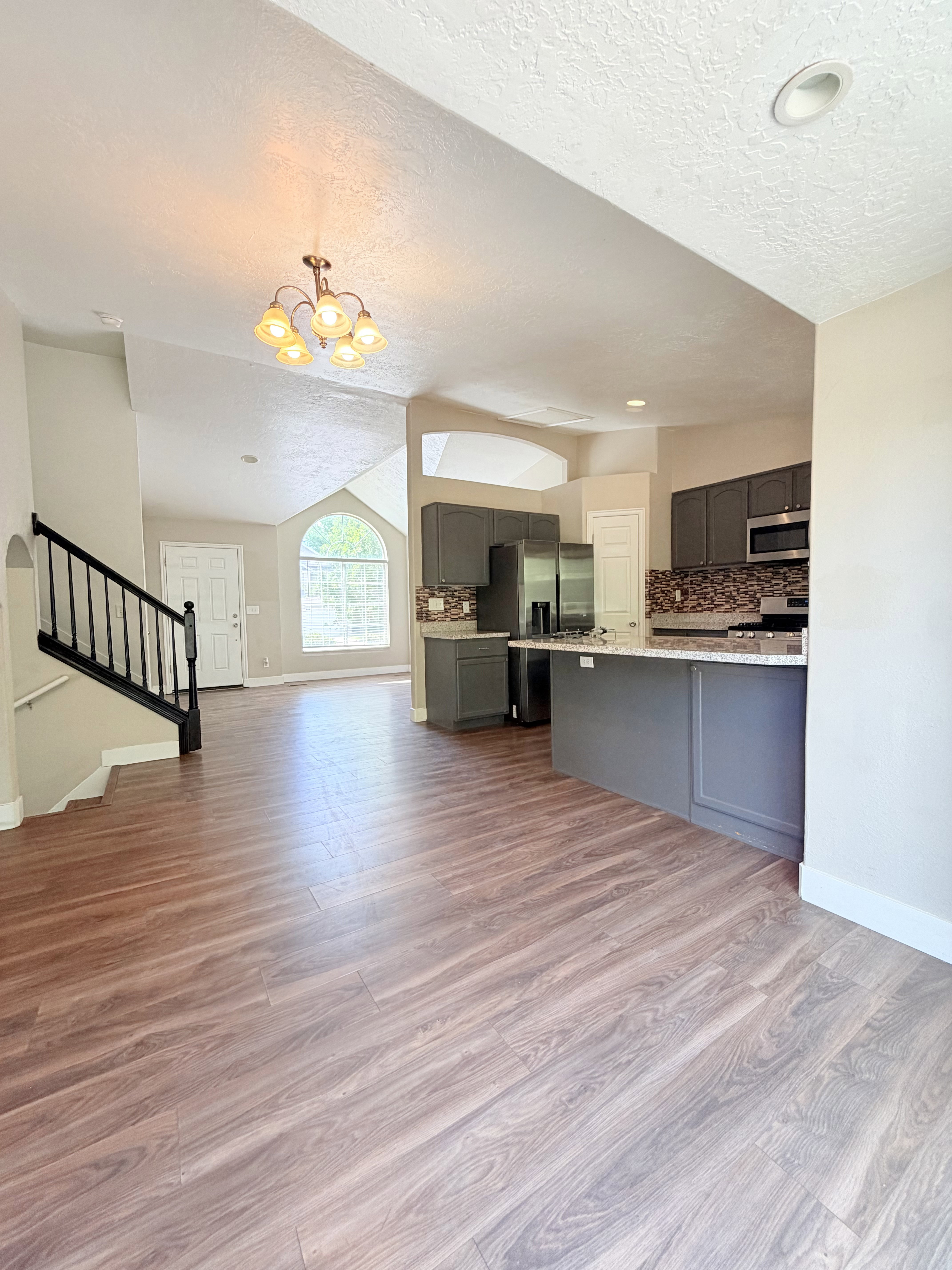 Open-concept living area featuring wood-finish flooring, a kitchen with grey cabinetry and light countertops, and a staircase with dark banisters