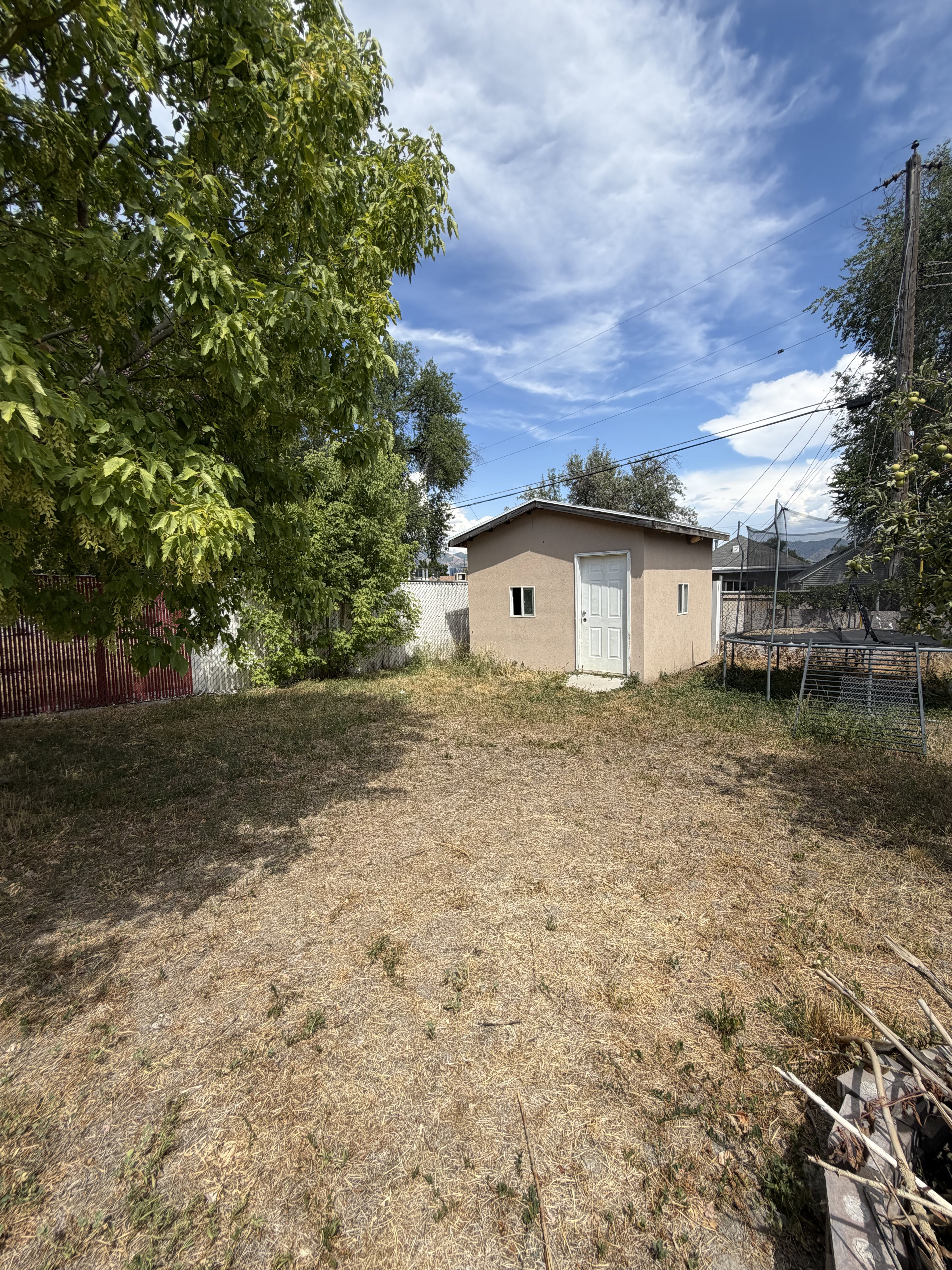 Spacious backyard featuring a detached storage shed, mature trees, and fencing