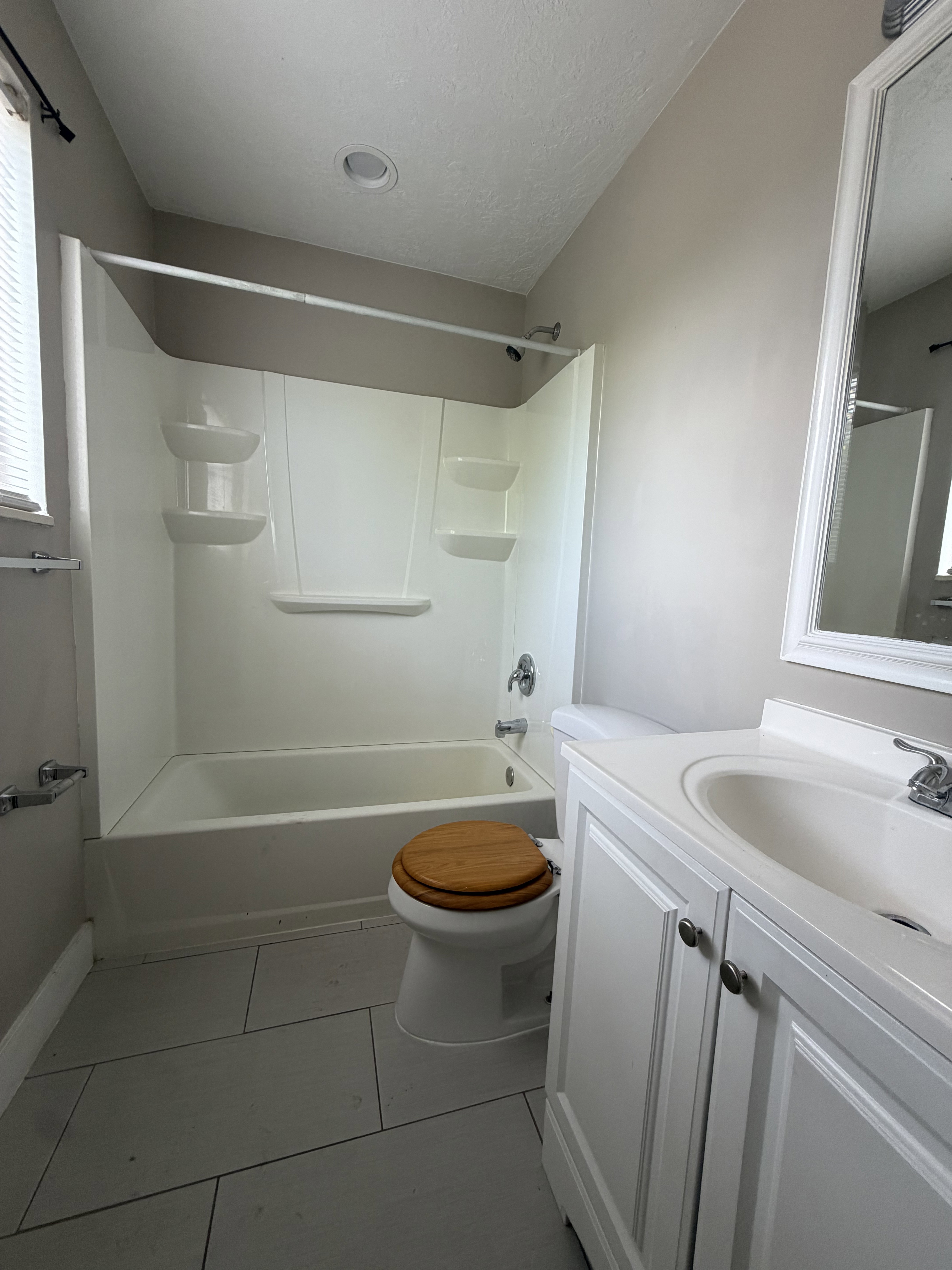 Bathroom featuring a white tub/shower combination, white vanity with integrated sink, chrome fixtures, and light-toned floor tiling