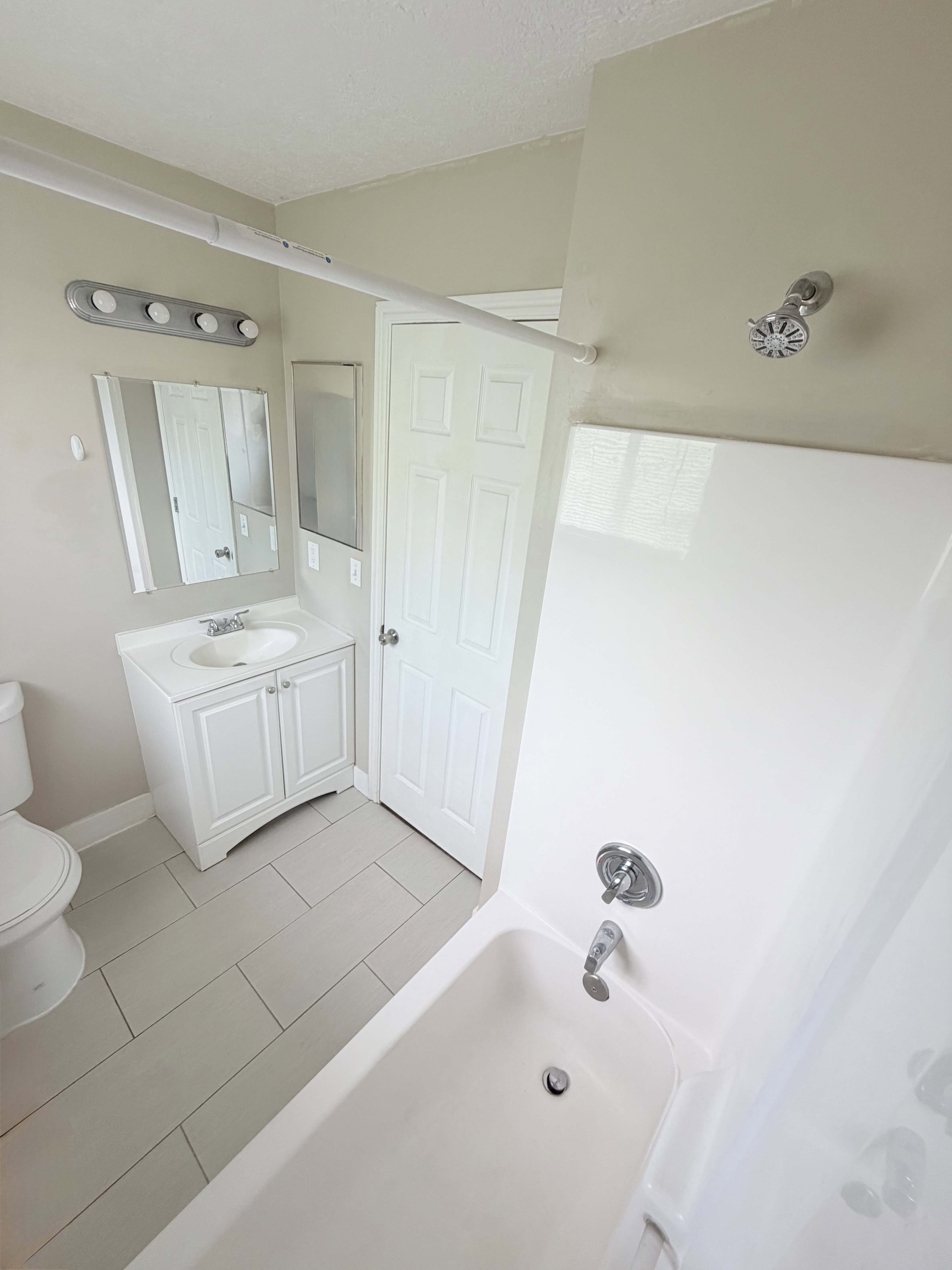 Bathroom featuring a white bathtub and shower combination with chrome fixtures, a single vanity with a white cabinet, and tile flooring