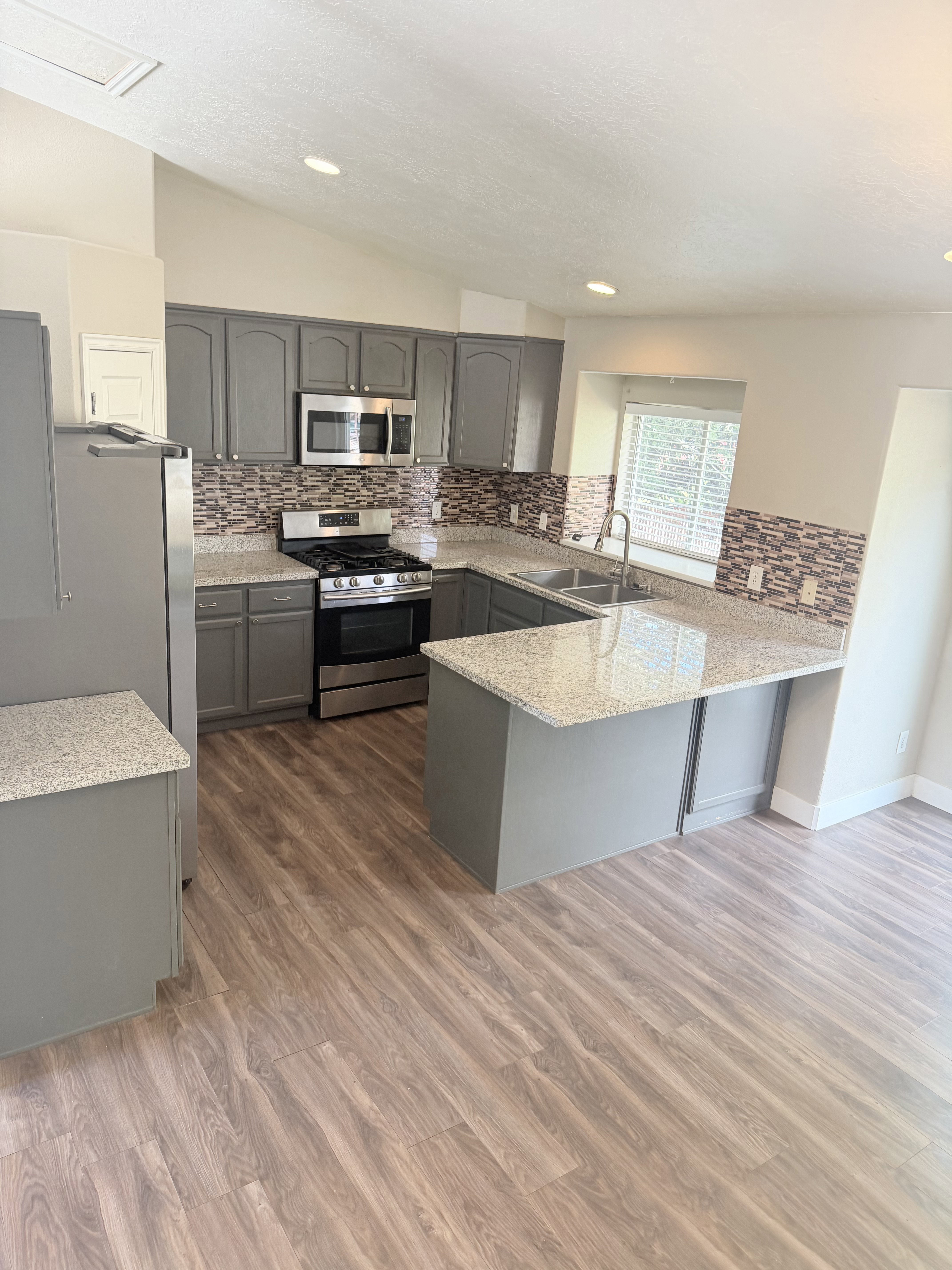 Kitchen featuring wood-finish flooring, grey cabinetry, granite-style countertops, mosaic tile backsplash, and stainless steel appliances