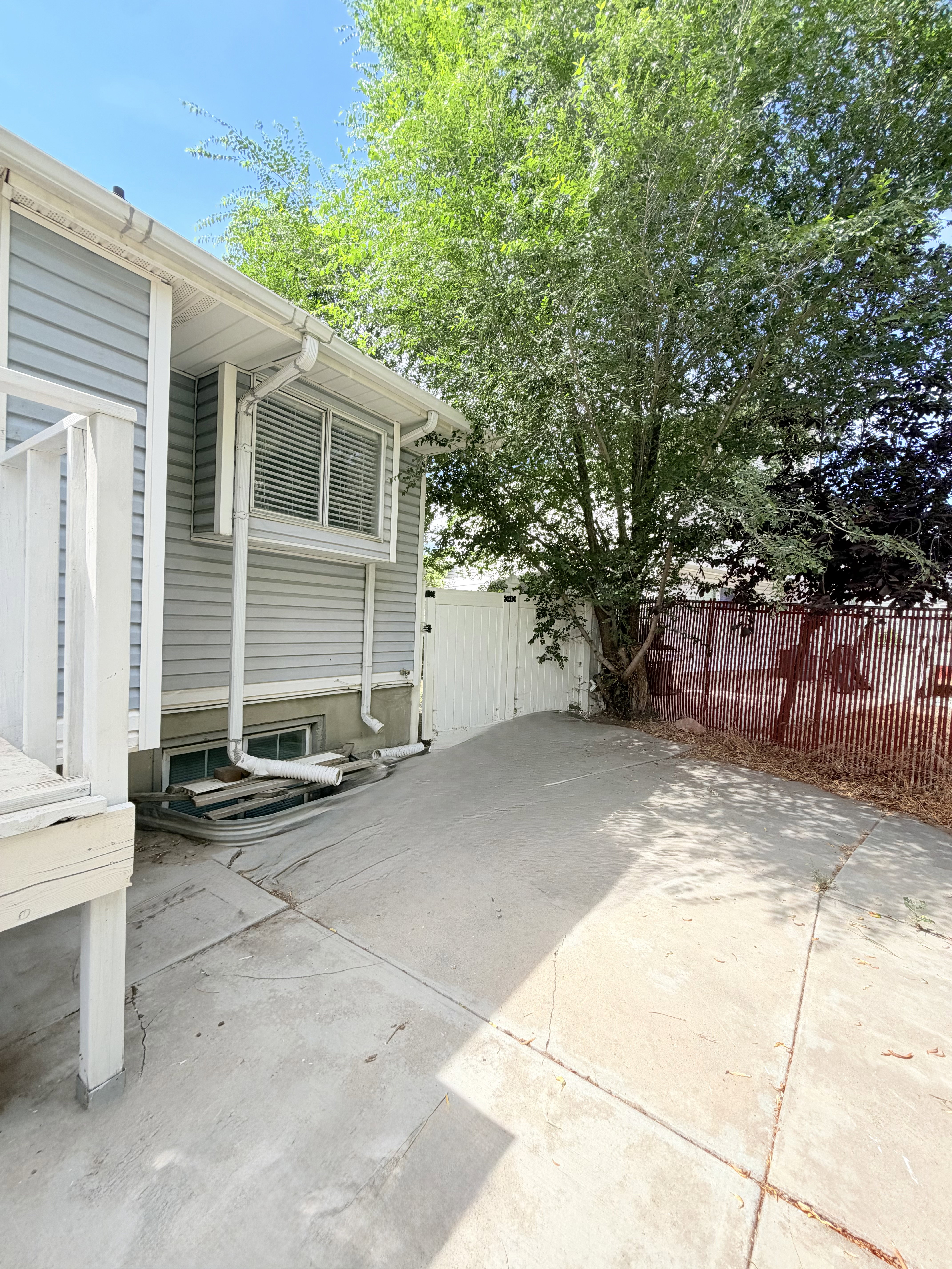Paved concrete patio featuring a white privacy fence and mature trees