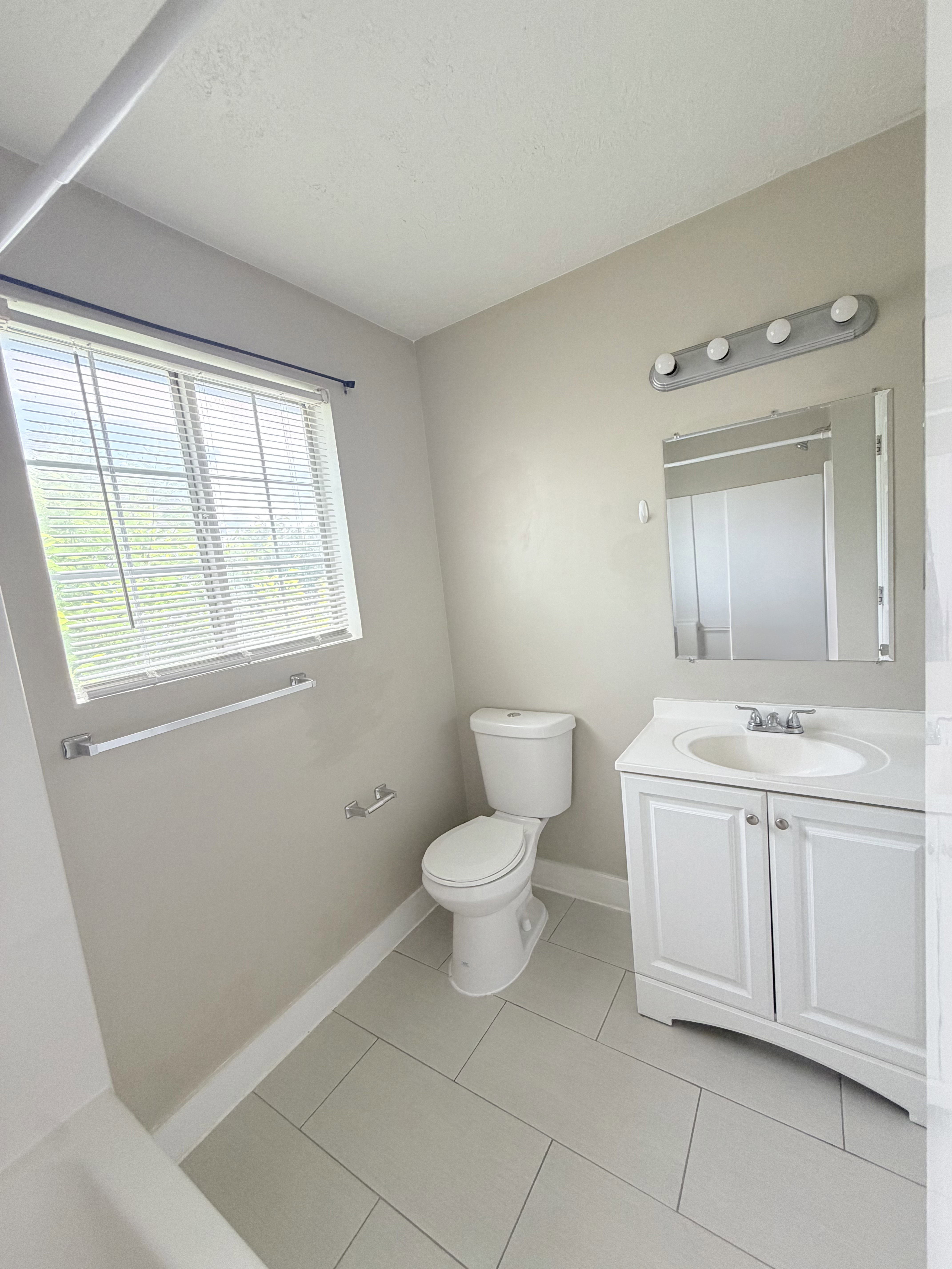 Bathroom with light gray tile flooring and a window with blinds