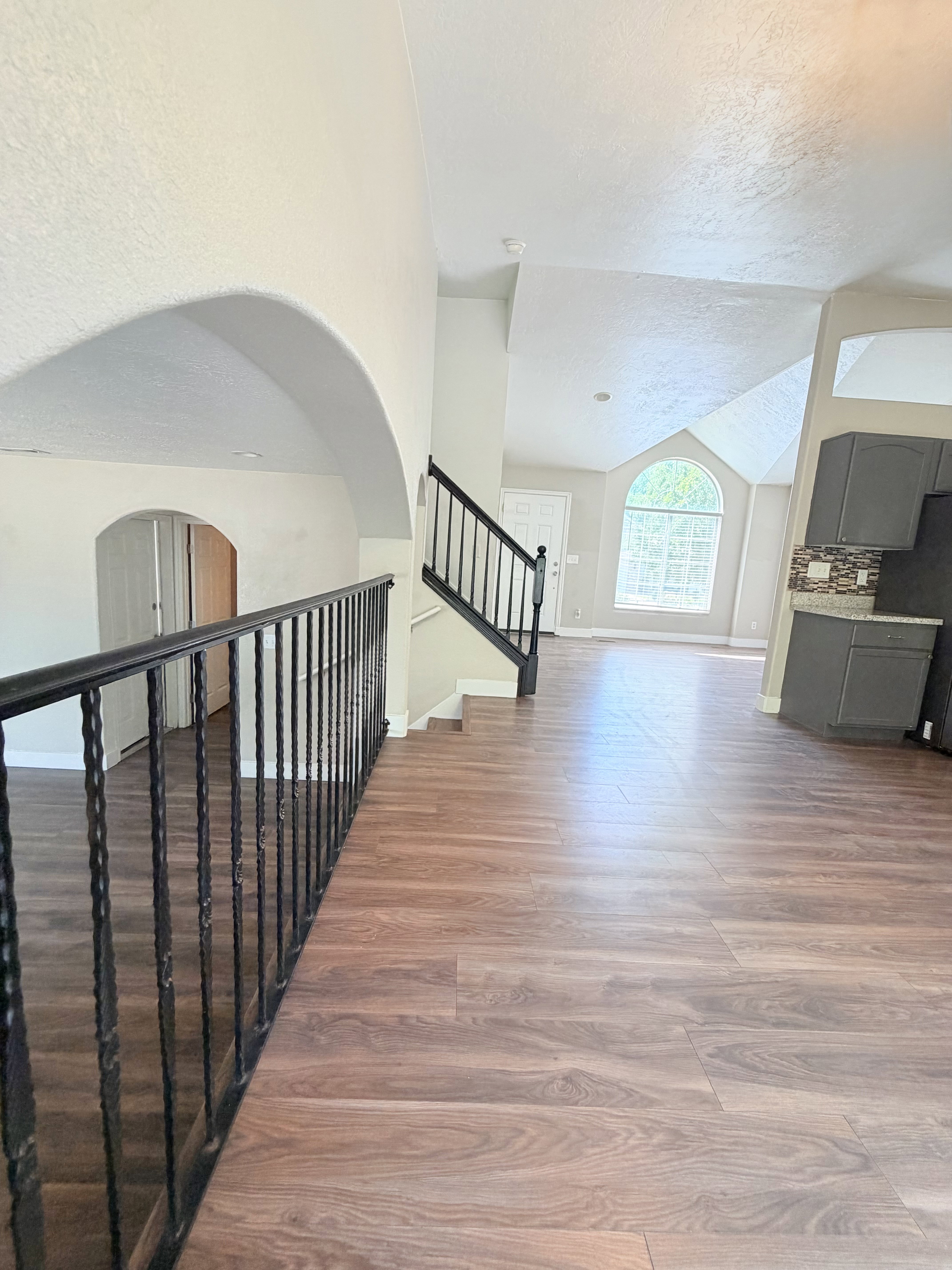 Open-concept interior featuring wood-finish flooring, a wrought iron railing, and arched architectural details