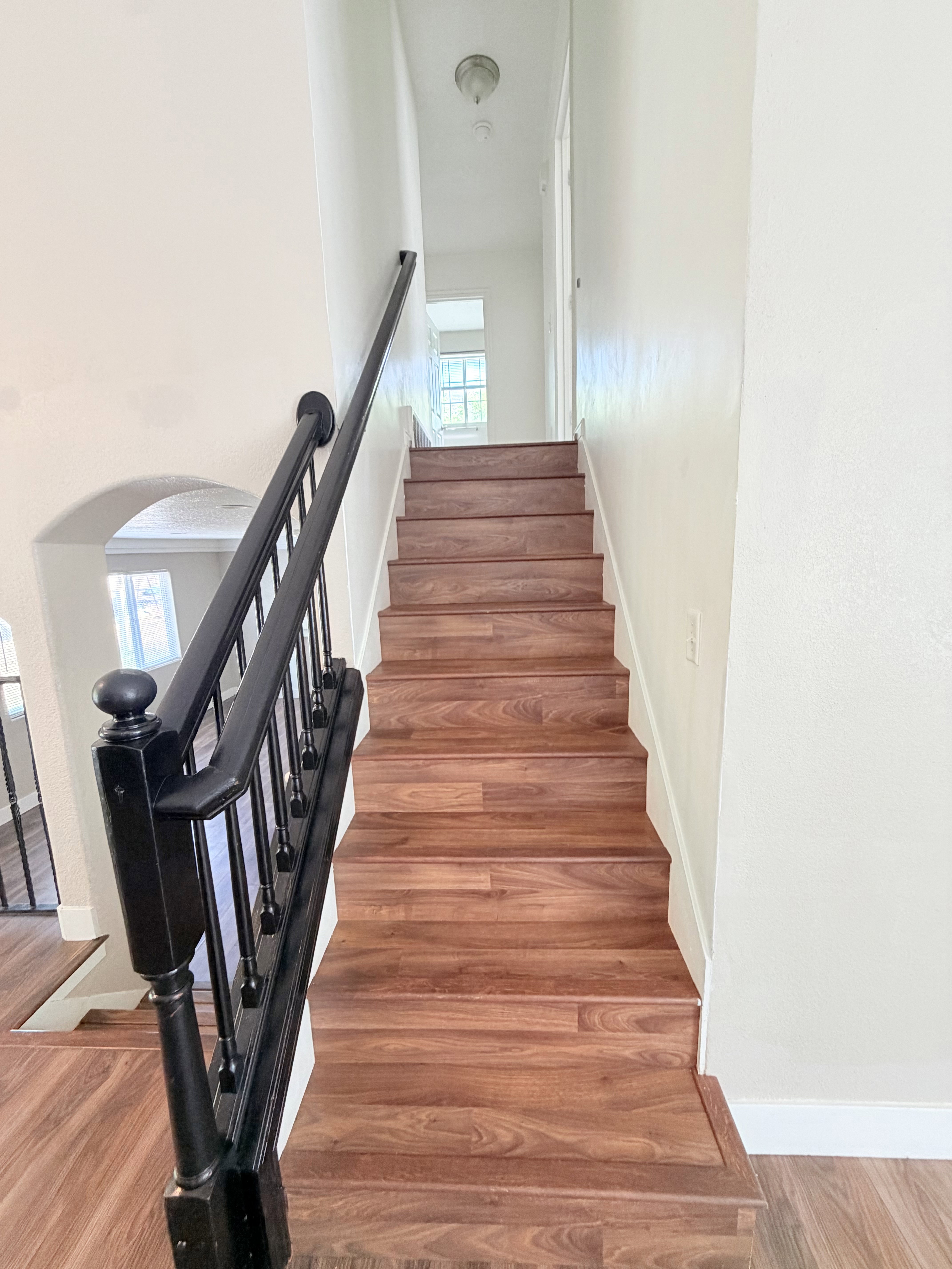 Staircase featuring wood-finish treads and risers, black painted handrail, and white painted balusters