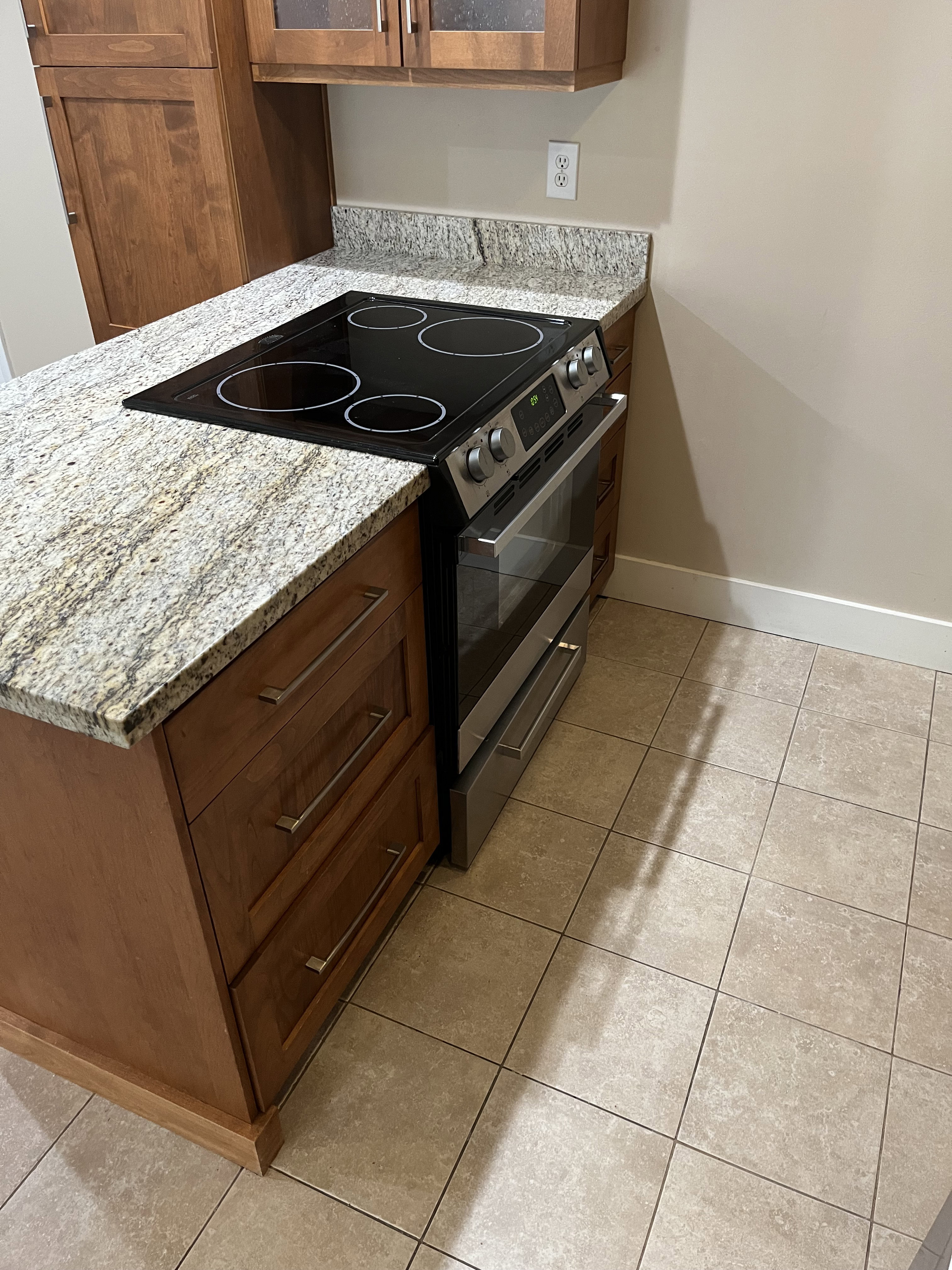 Integrated stainless steel range with a ceramic cooktop set into a light-toned granite countertop