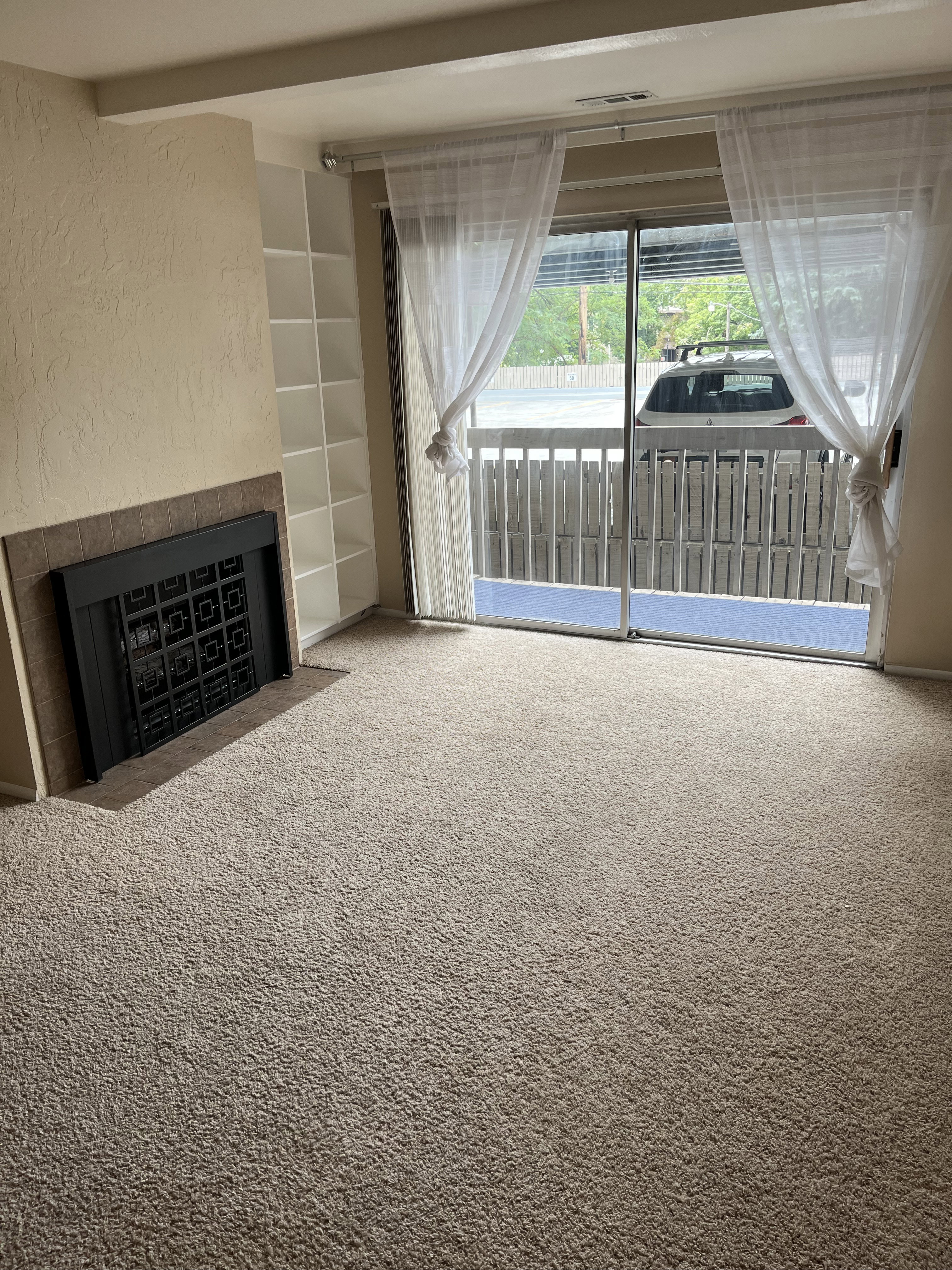 Living area featuring a sliding glass door to an exterior balcony, built-in shelving, a fireplace with a dark metal insert, and neutral-toned carpeting