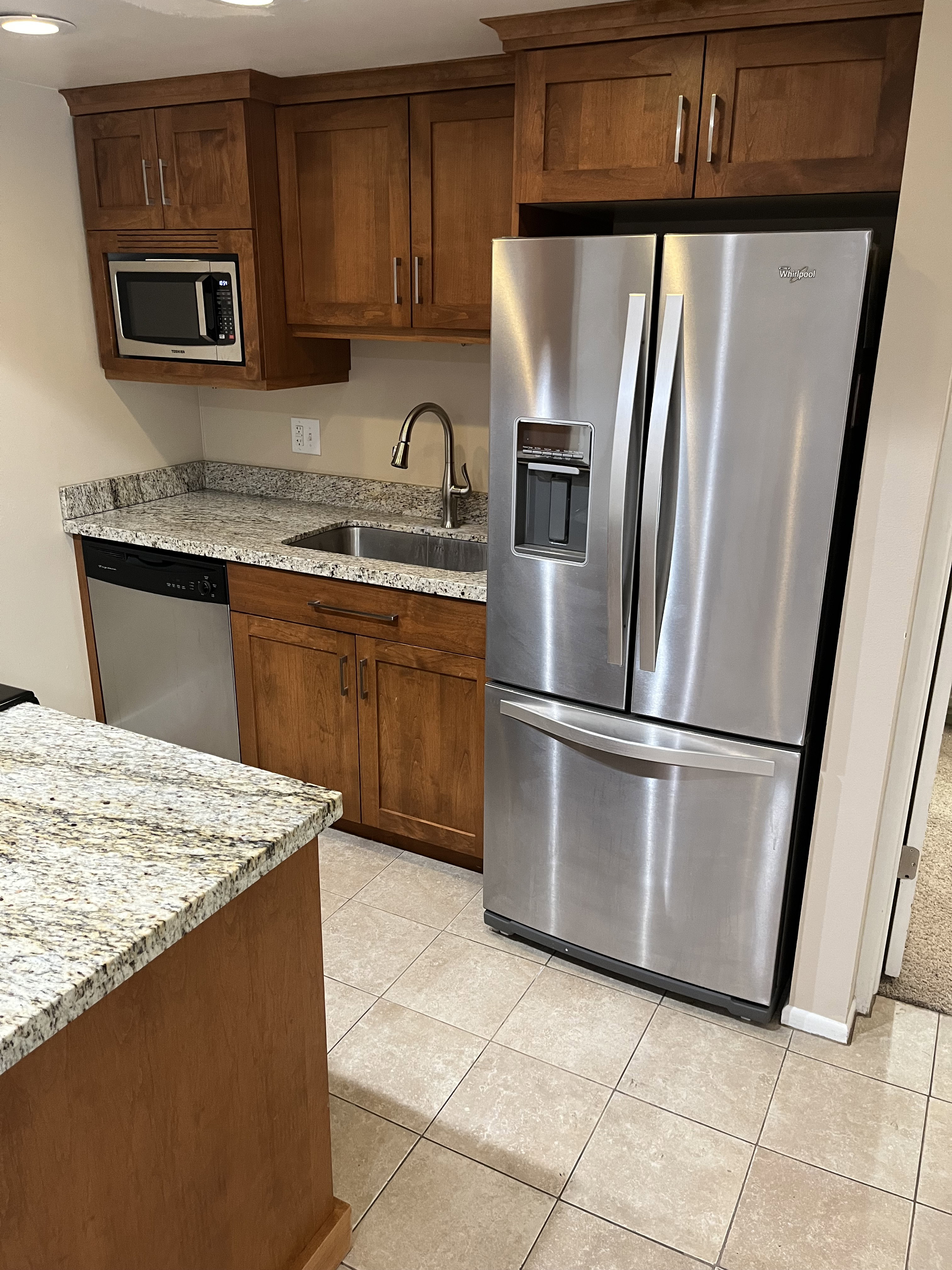 Kitchen featuring wood cabinetry, stainless steel appliances, granite countertops, and tiled flooring