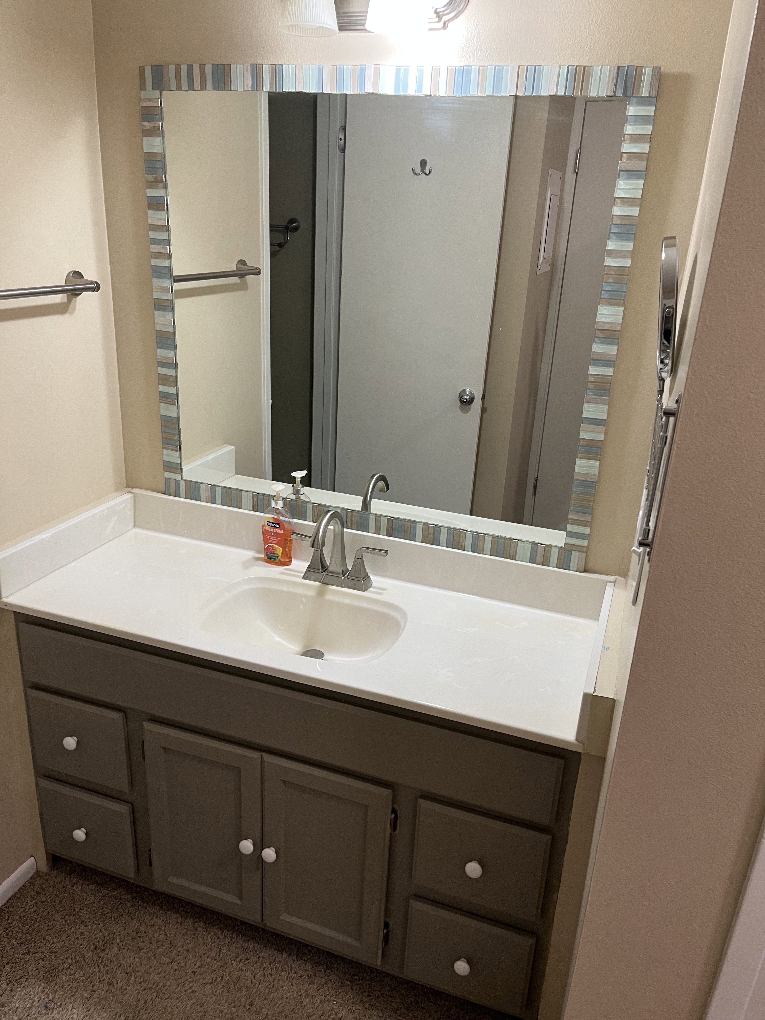 Bathroom vanity featuring a light-colored countertop with an integrated sink, a gray cabinet with white knobs, and a framed mirror with a horizontal stripe pattern