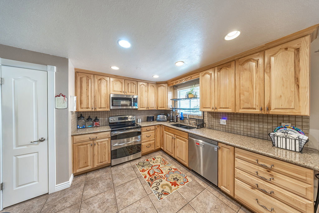 Kitchen featuring light wood cabinetry, stone-finish countertops, stainless steel appliances, and a tiled backsplash