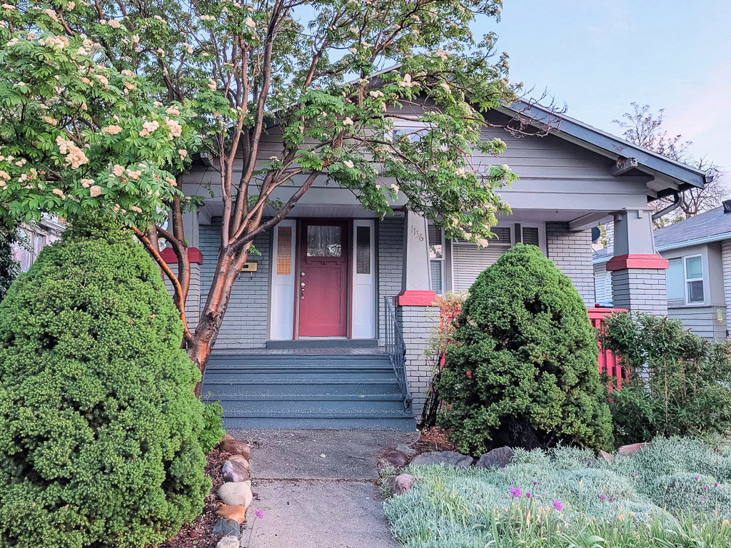 Charming bungalow exterior with a covered porch, brick detailing, and a vibrant red entry door