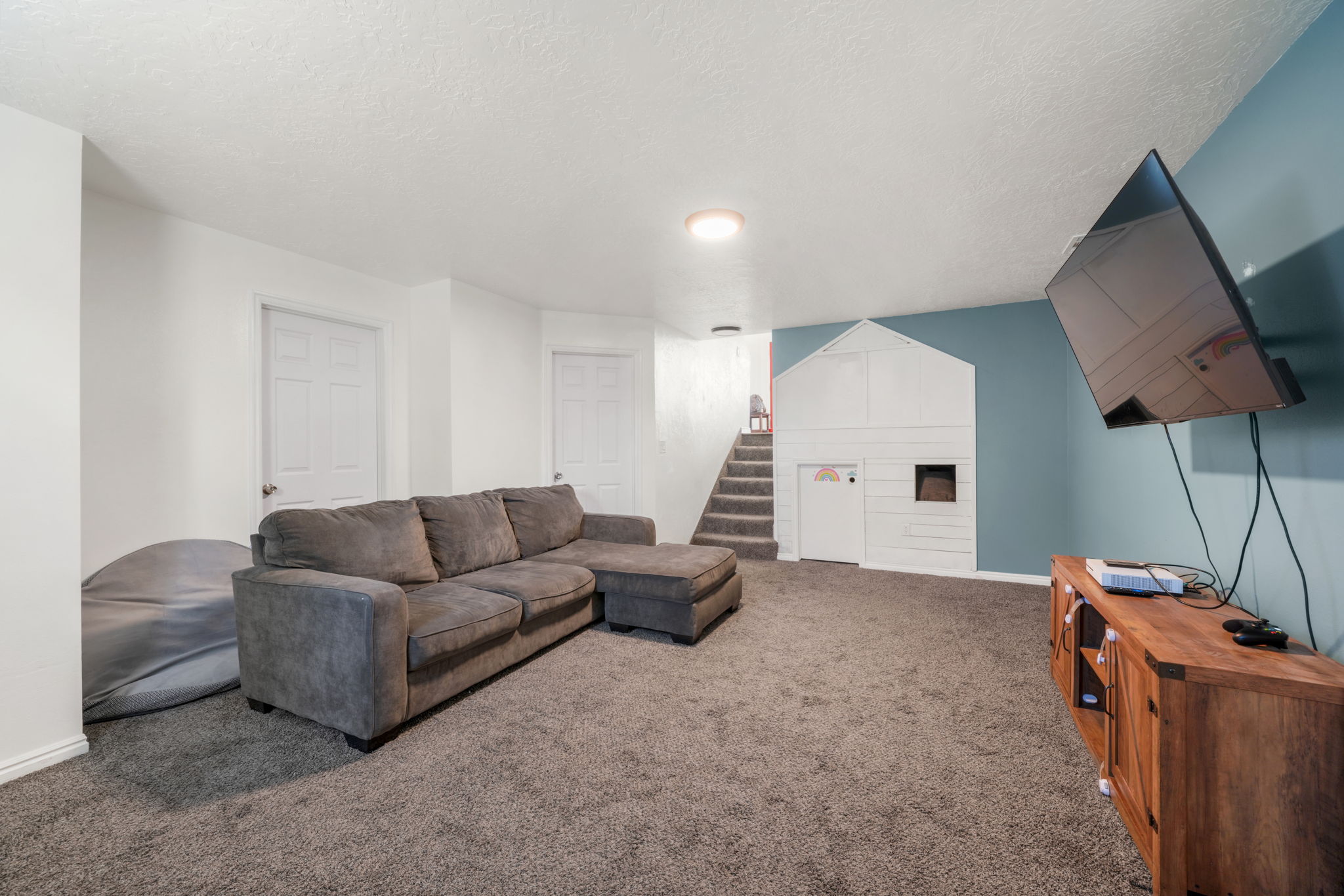 Carpeted recreation room featuring white walls, a blue accent wall, and a built-in play structure