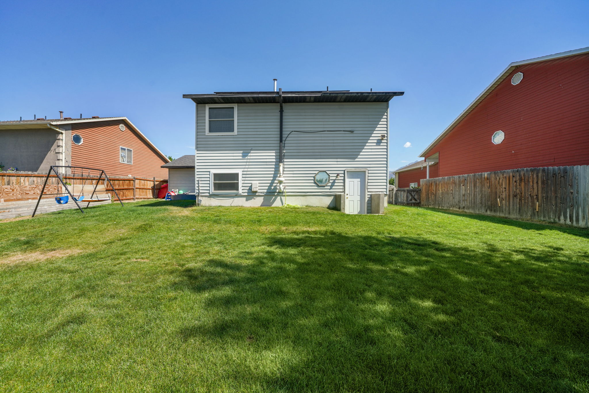 Expansive grassy yard with a wooden fence boundary, and a two-story residence featuring light-colored siding and a lower-level access door