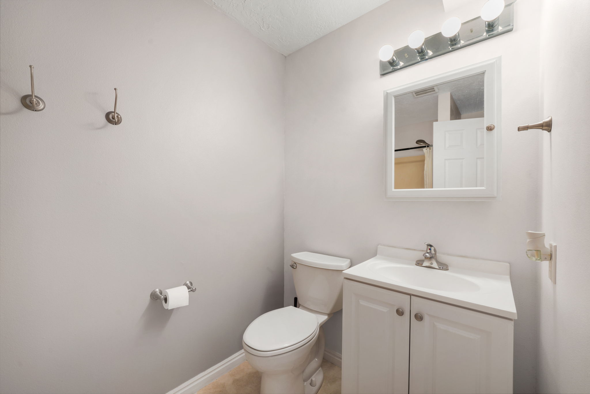 Bathroom featuring a white vanity with integrated sink, chrome faucet, wall-mounted mirror, and overhead vanity lighting