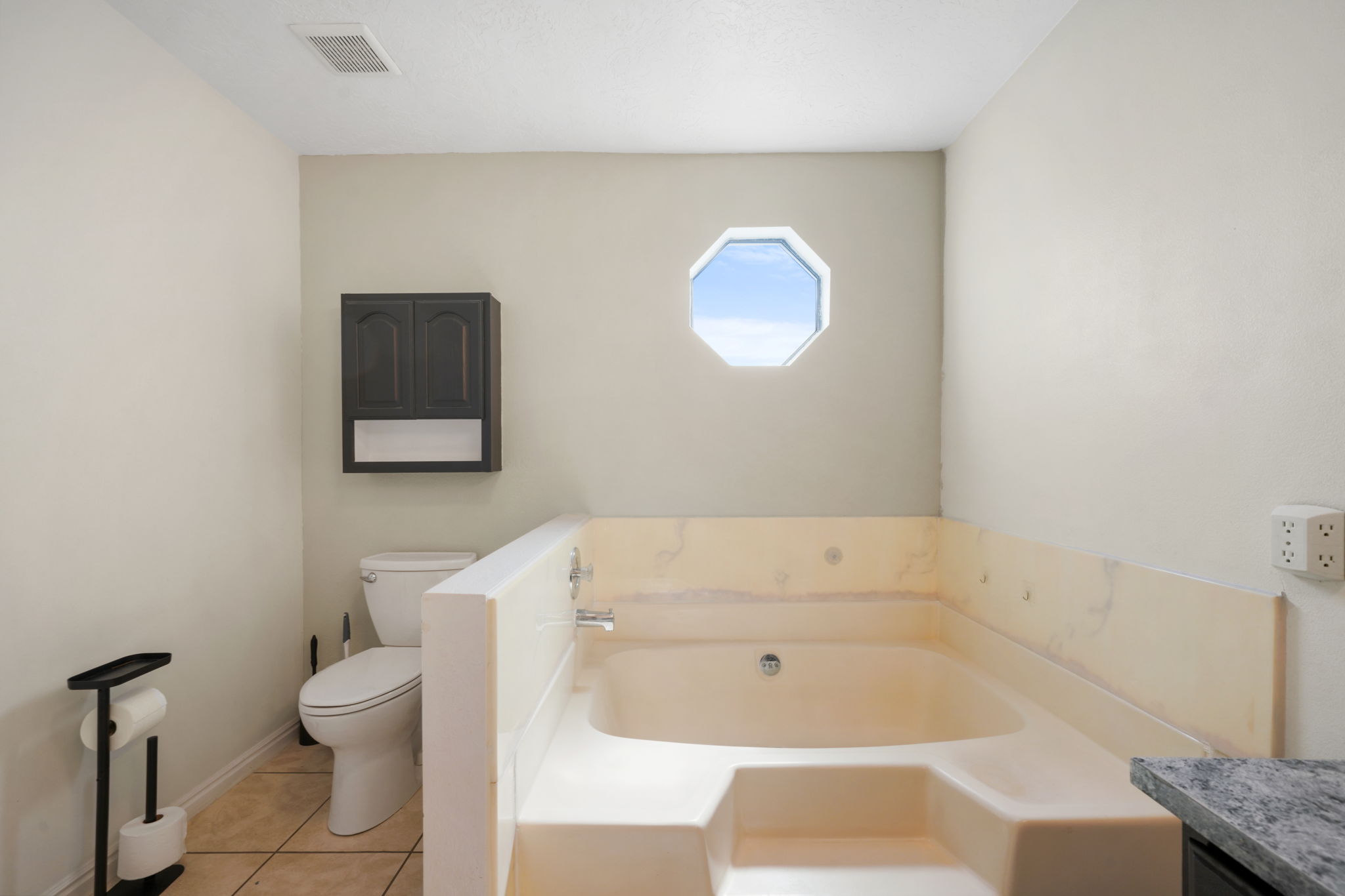 Built-in tub with integrated steps, octagonal window, and wall-mounted storage cabinet